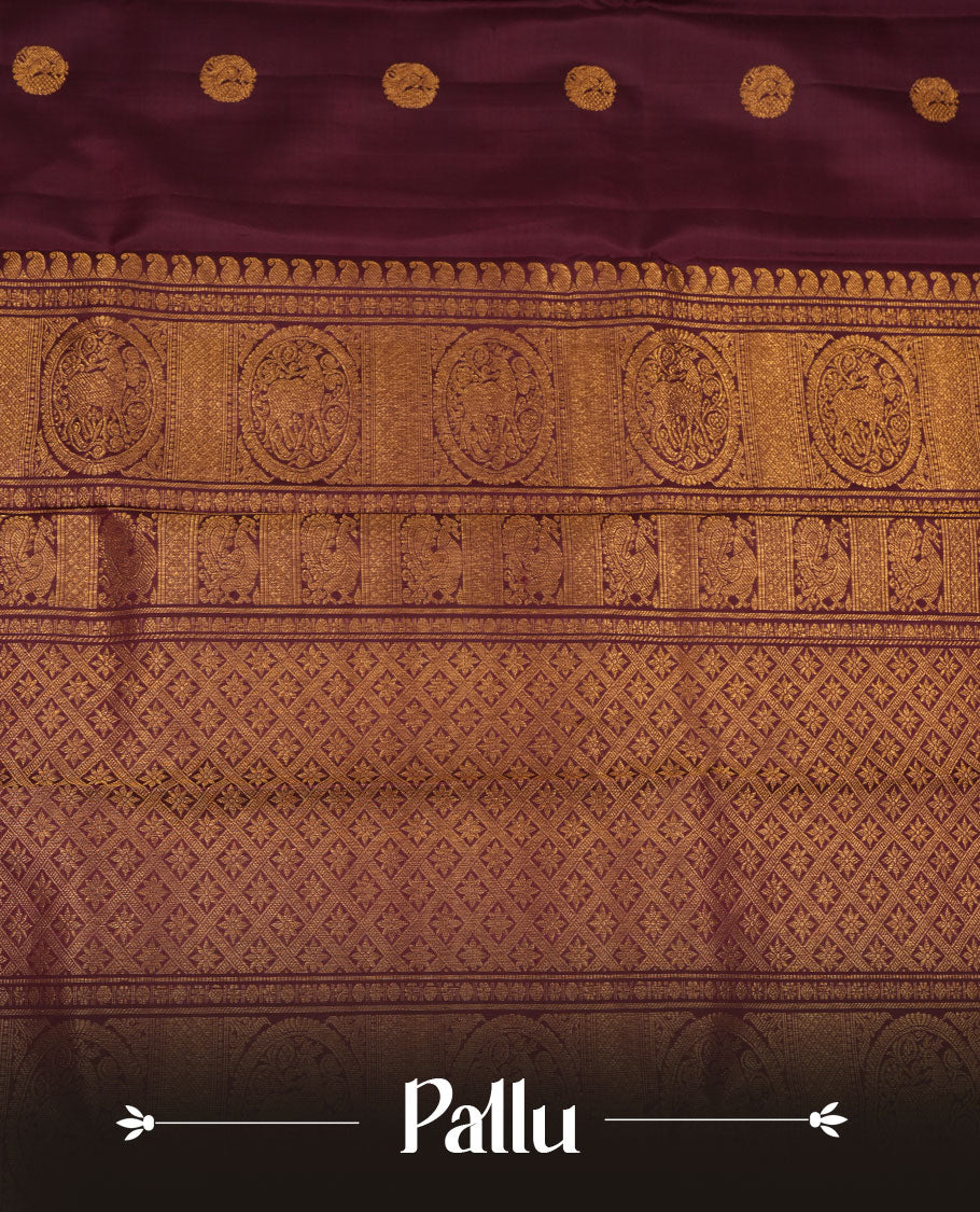 Dark chocolate colour pure traditional Kancheepuram silk saree adorned with elegant peacock and chakra motifs across the body, featuring rich gold zari traditional borders, beautifully paired with a matching blouse piece.