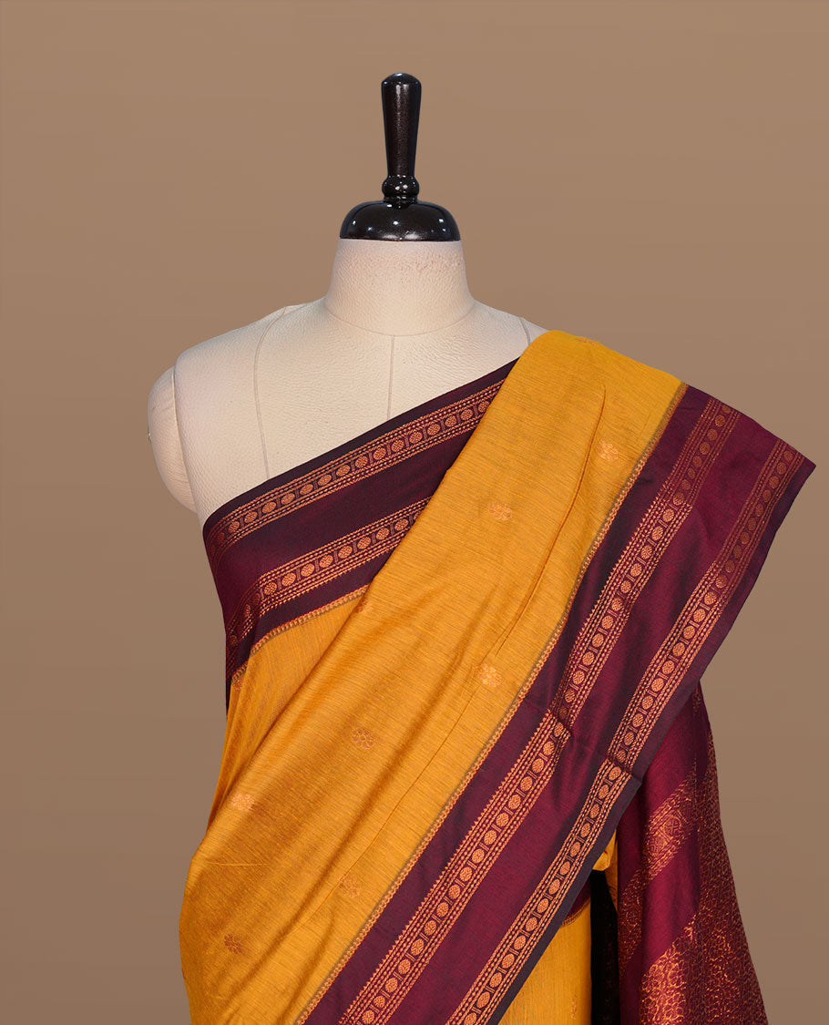Mustard colour kalyani cotton saree featuring gold zari motifs on body, complemented by contrast maroon color with copper zari pattern border , paired with mtaching blouse piece.