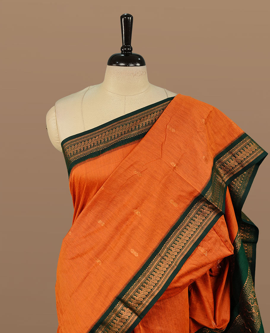 Rust orange colour kalyani cotton saree featuring gold zari motifs on body, complemented by green colour with zari border, paired with matching blouse piece.