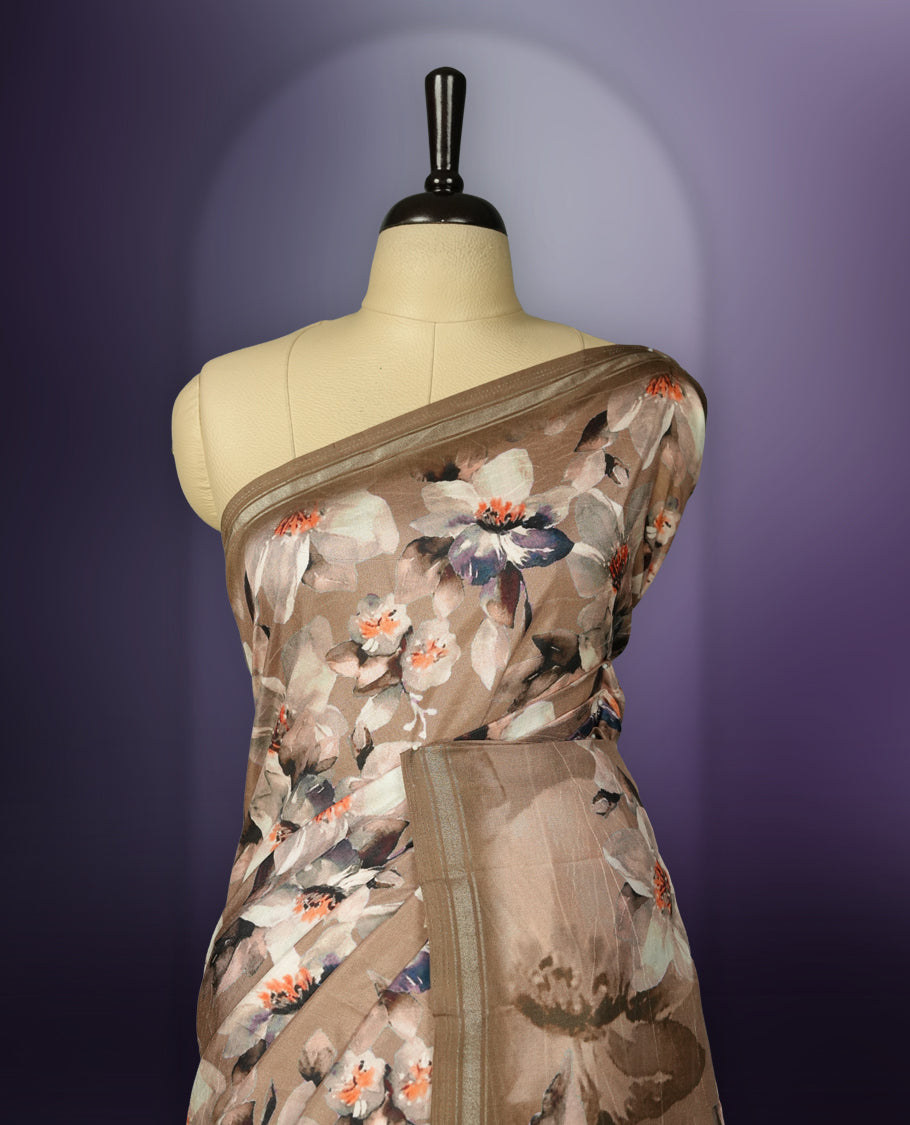 Pastel brown colour saree adorned with elegant floral prints on the body, enhanced with a subtle matching border, complemented by a beautifully printed pallu featuring blooming flowers, and paired with a matching blouse.
