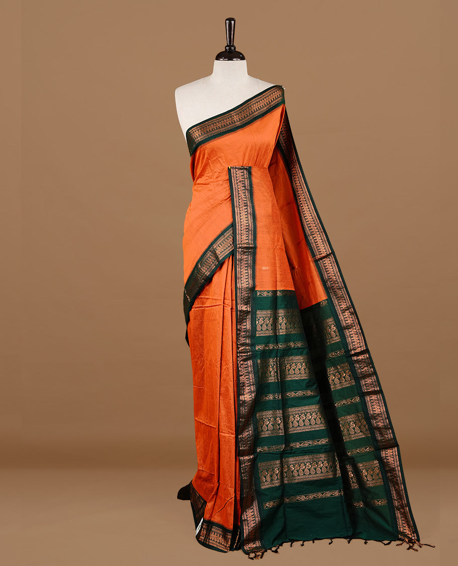 Orange colour kalyani cotton saree featuring gold zari motifs on body, highlighting contrast green colour with Antique gold zari border, paired with matching blouse piece.