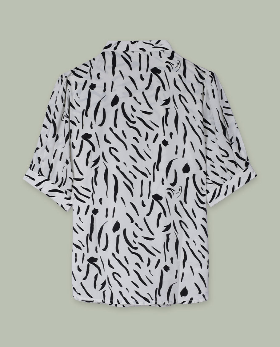 White and black abstract printed shirt top with notched lapel collar, single visible button at front, elbow-length sleeves, and softly gathered shoulders.