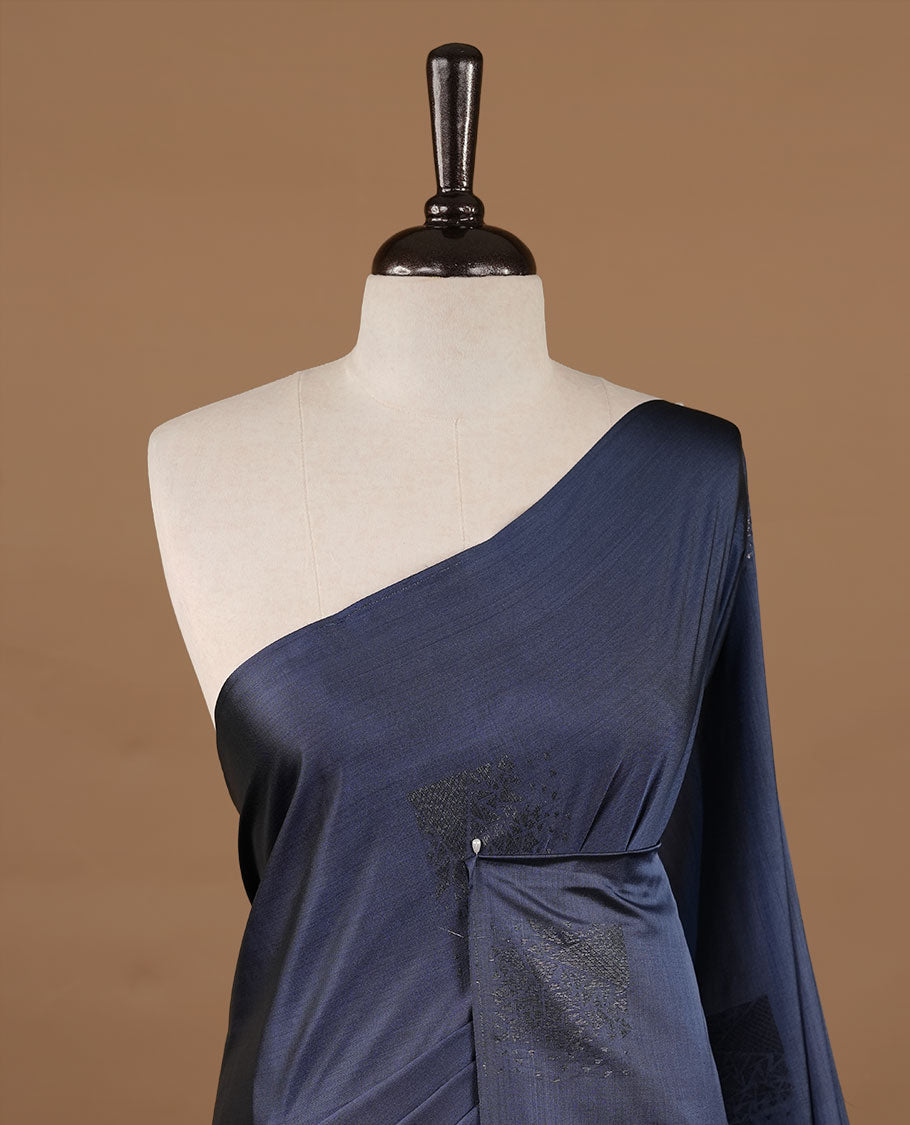 Navy blue colour soft silk saree features a sleek borderless design with intricate antique zari motifs, flowing into a striking contrast rust orange pallu and a matching blouse piece.