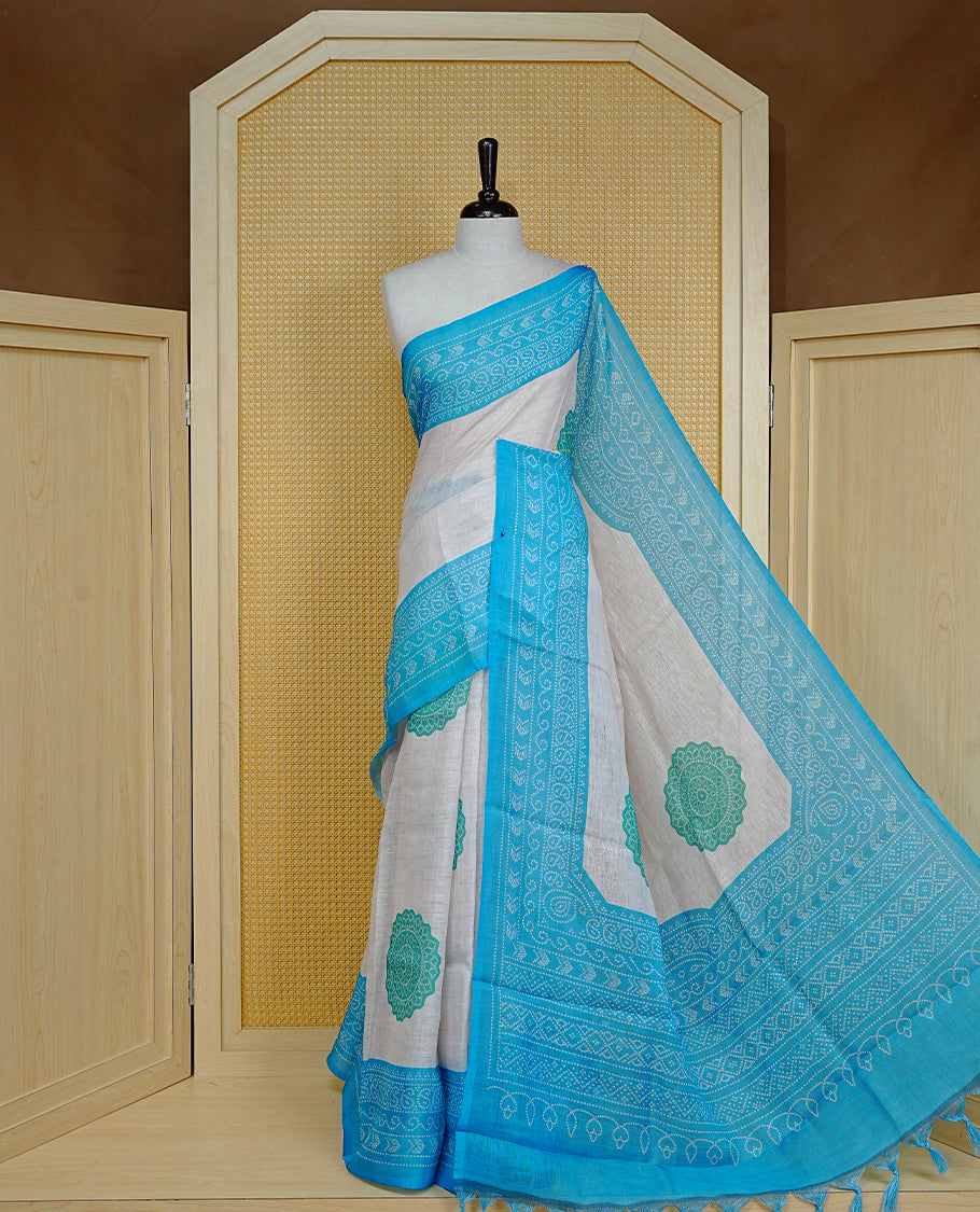 Cream colour semi linen saree featuring Green Ajrakh pattern print on body, complemented by contrast Blue colour with same pattern print border, comes with matching blouse piece.