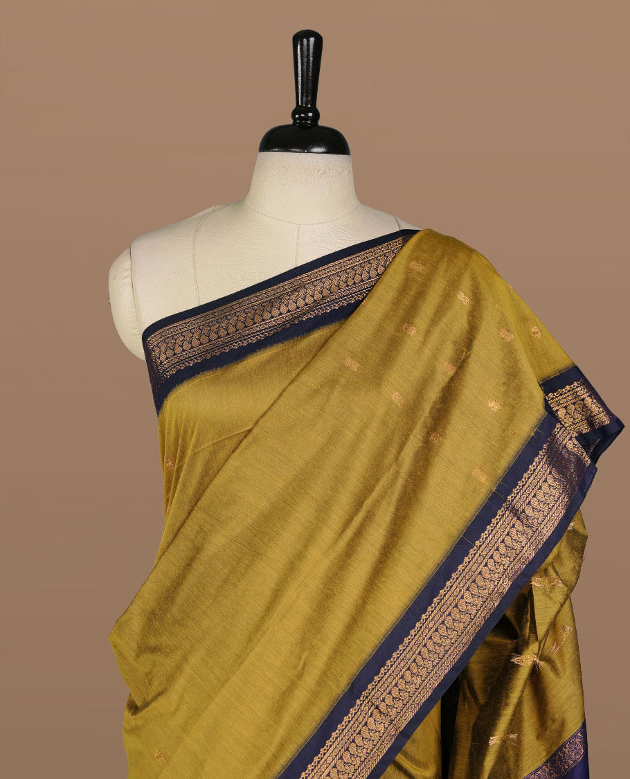 Olive colour kalyani cotton saree featuring antique zari motifs on body, complemented by Dark blue colour with Antique zari border, paired with matching blouse piece.