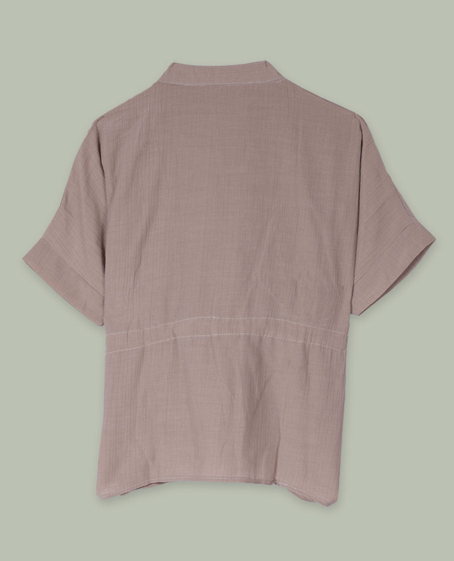 Taupe short-sleeve top with V-slit band neckline, contrast white crochet motif on one side, and adjustable drawstring detail at the waist