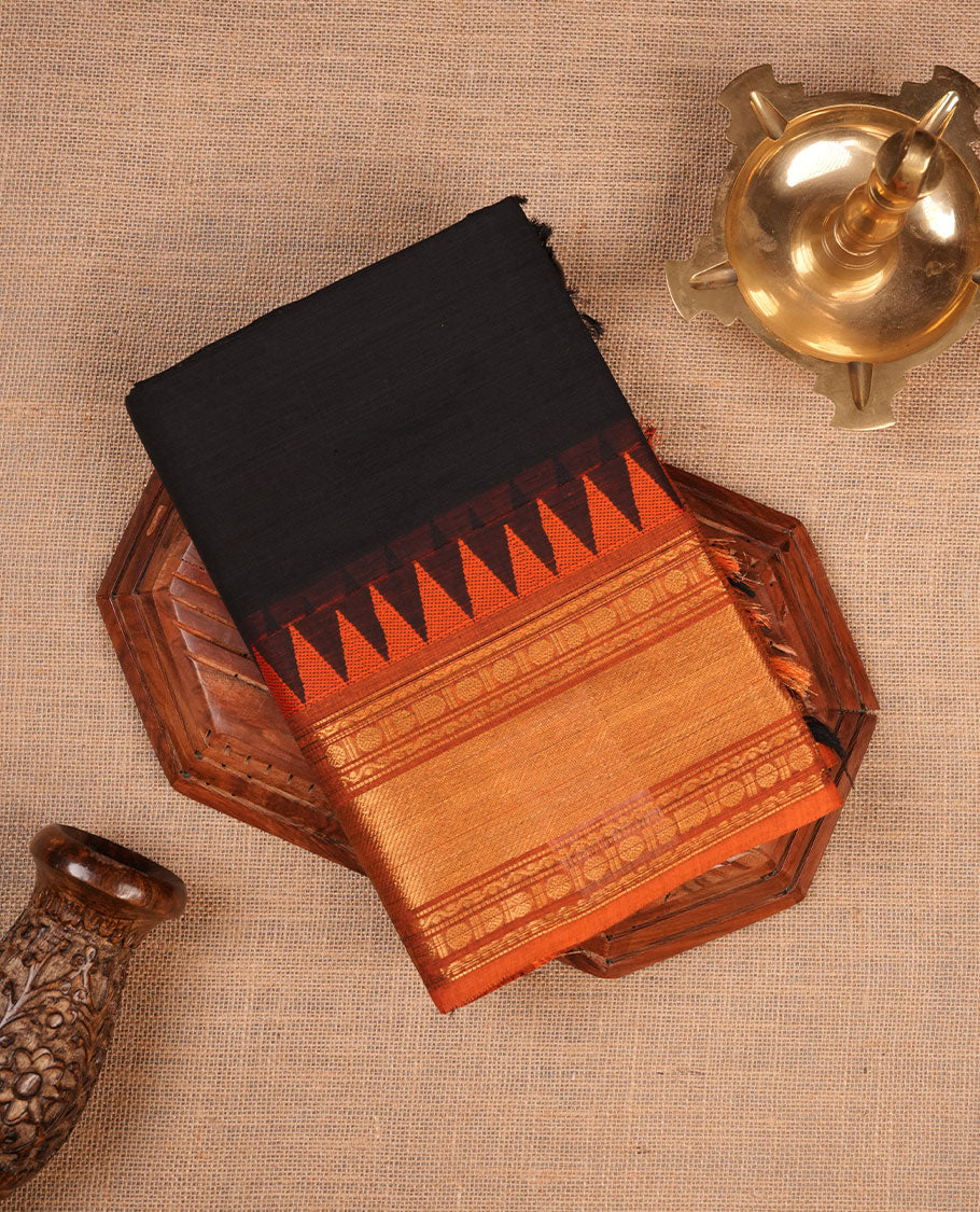 Black colour chettinad cotton saree featuring Elegant plain body highlighting contrast orange colour colour with gold zari traditional border, pallu and paired with matching blouse piece.