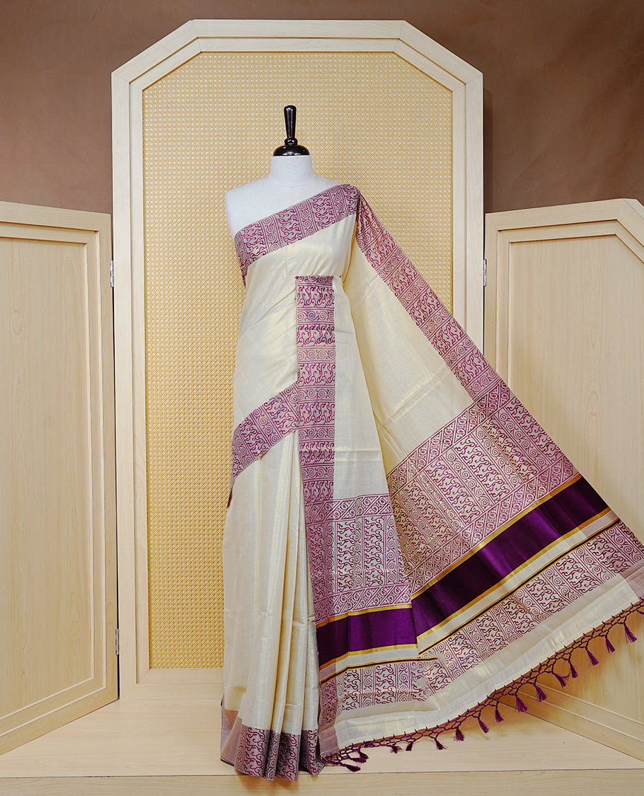 Cream Colour Tissue Kerala Saree Featuring a Plain Body, Enhanced with Violet Block Printed Borders, a Violet and Gold Zari Pallu, Violet Tassels, and a Matching Blouse Piece.