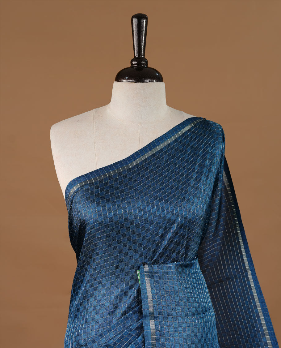 Peacock blue colour Semi Tussar saree featuring an elegant zari fancy check pattern on the body, highlighted with a small border for a refined look. Comes without a blouse piece.
