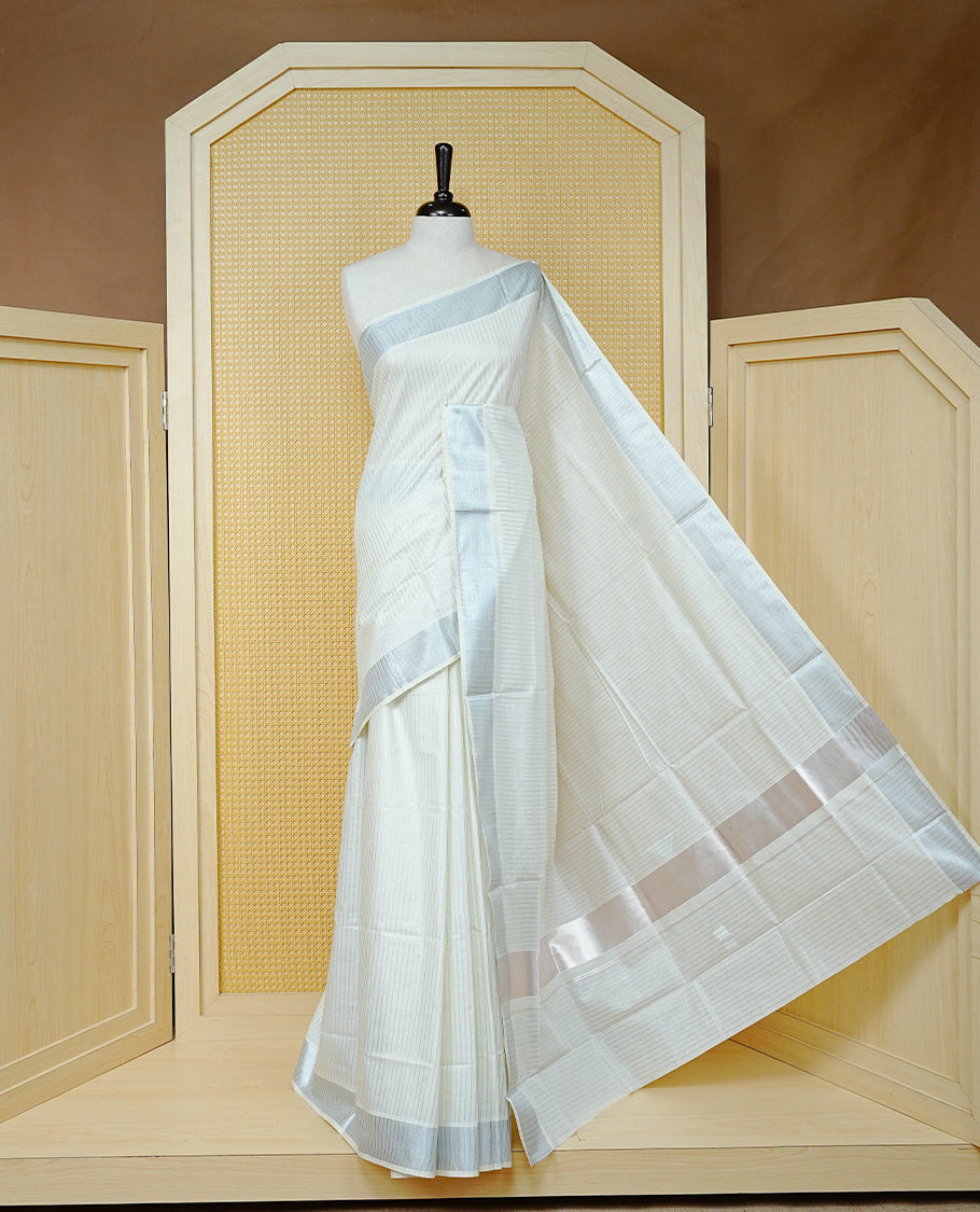 Cream colour Cotton kerala saree featuring Silver zari Stripes on body, complemented by Silver Zari Border & Rose gold zari Pallu, paired with matching blouse piece.