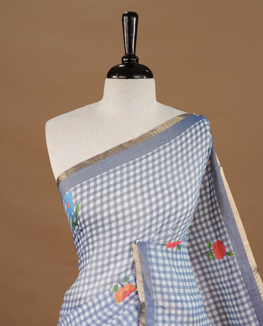Grey colour Semi Linen saree featuring a stylish check pattern adorned with floral prints on the body, enhanced by a small gold border, paired with a matching blouse piece.