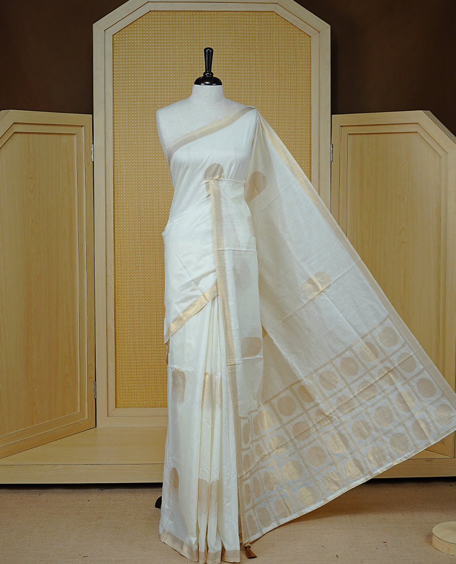 Cream Colour Organza Kerala Saree Featuring Gold Zari Buttas On The Body, Enhanced By A Gold Zari Border & Geometric Design Pallu, Paired With A Matching Blouse Piece.