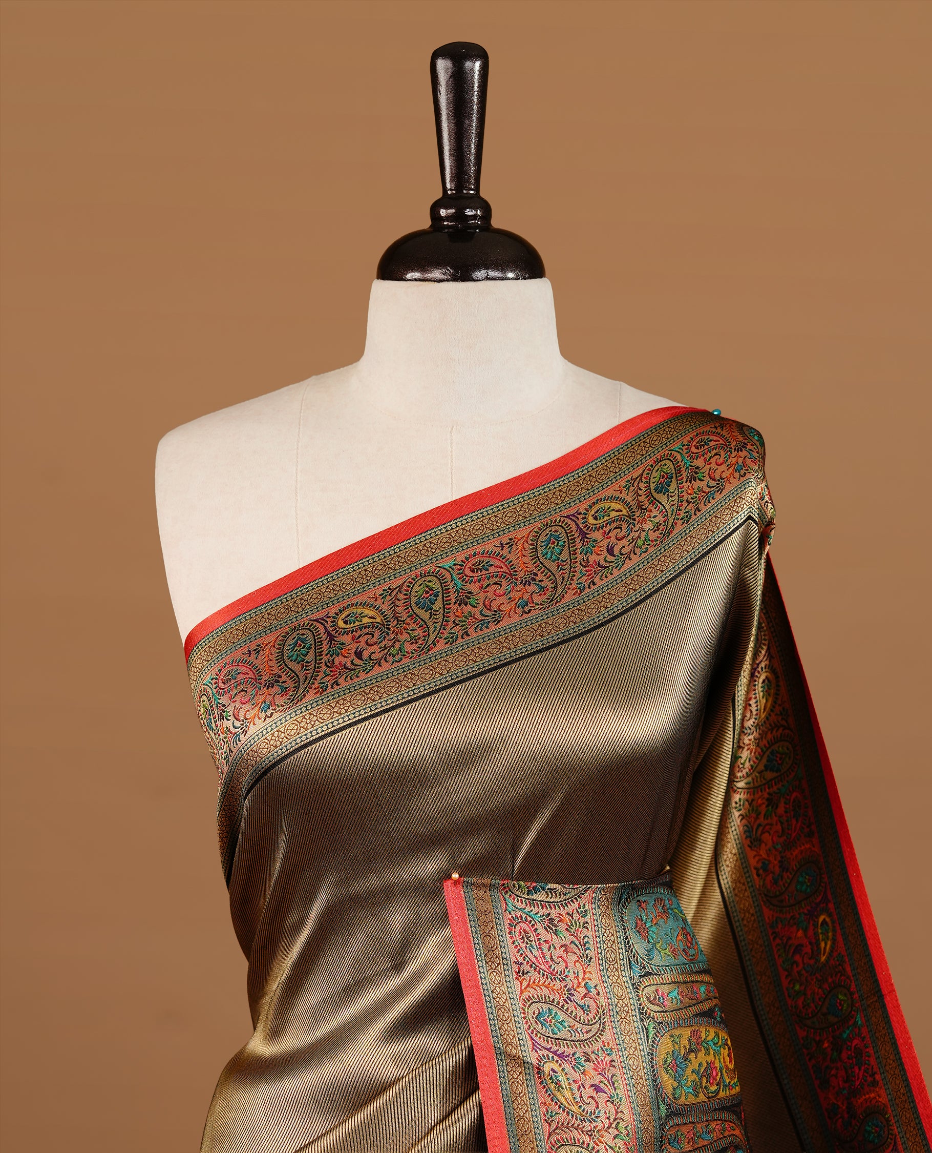 Bronze colour Pashmina Saree featuring a plain self textured body, a multicolour paisley woven border with red edging, an ornate multicolour paisley woven pallu, paired with a contrast red blouse with a matching woven border.