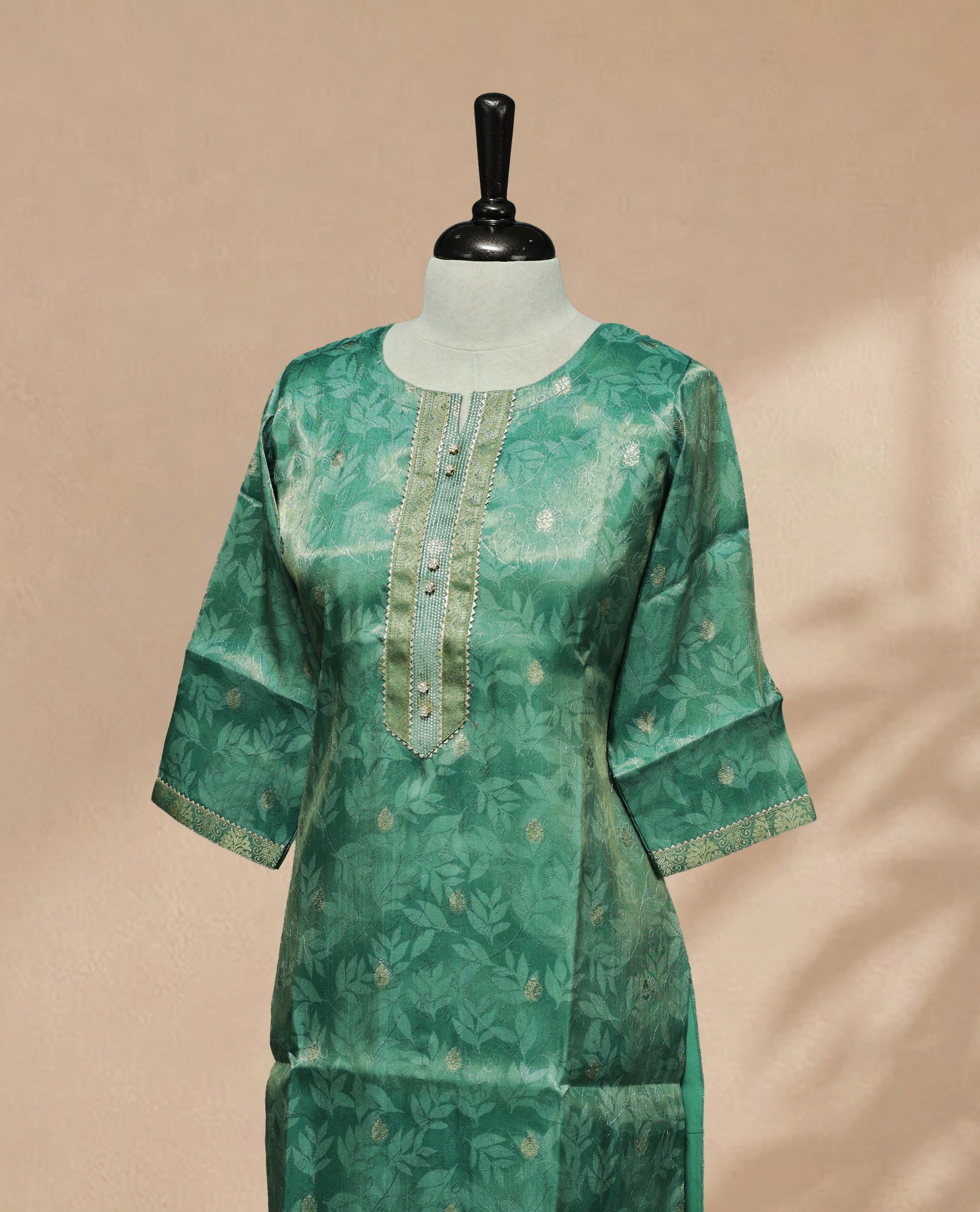 Green colour tissue Kurti featuring a delicate floral leaf pattern with subtle gold motifs, a round neckline adorned with intricate thread and Stone detailing, and 3/4 sleeves finished with matching embroidered borders.