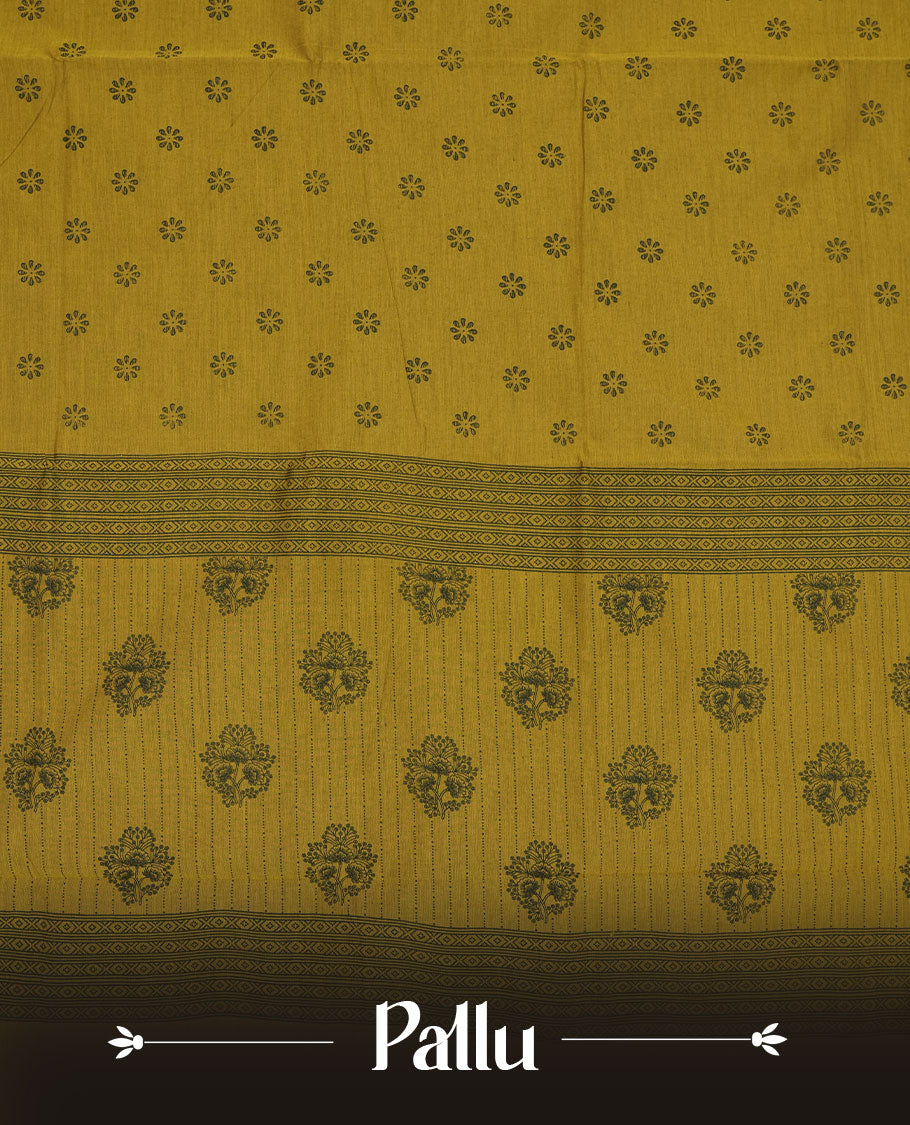 Dark Mustard colour poly cotton saree with black floral butti motifs on the body, paired with a matching pallu featuring black ornate floral jaal and stripes on the border, and a coordinated all‑over black paisley printed blouse piece.