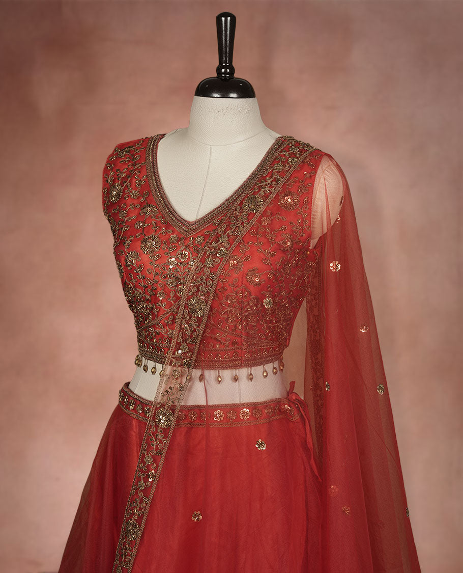Red colour lehenga set with stitched sleeveless Antique thread embroidered & beats worked blouse featuring sheer neckline, matching stitched flared lehenga, and plain sheer dupatta.