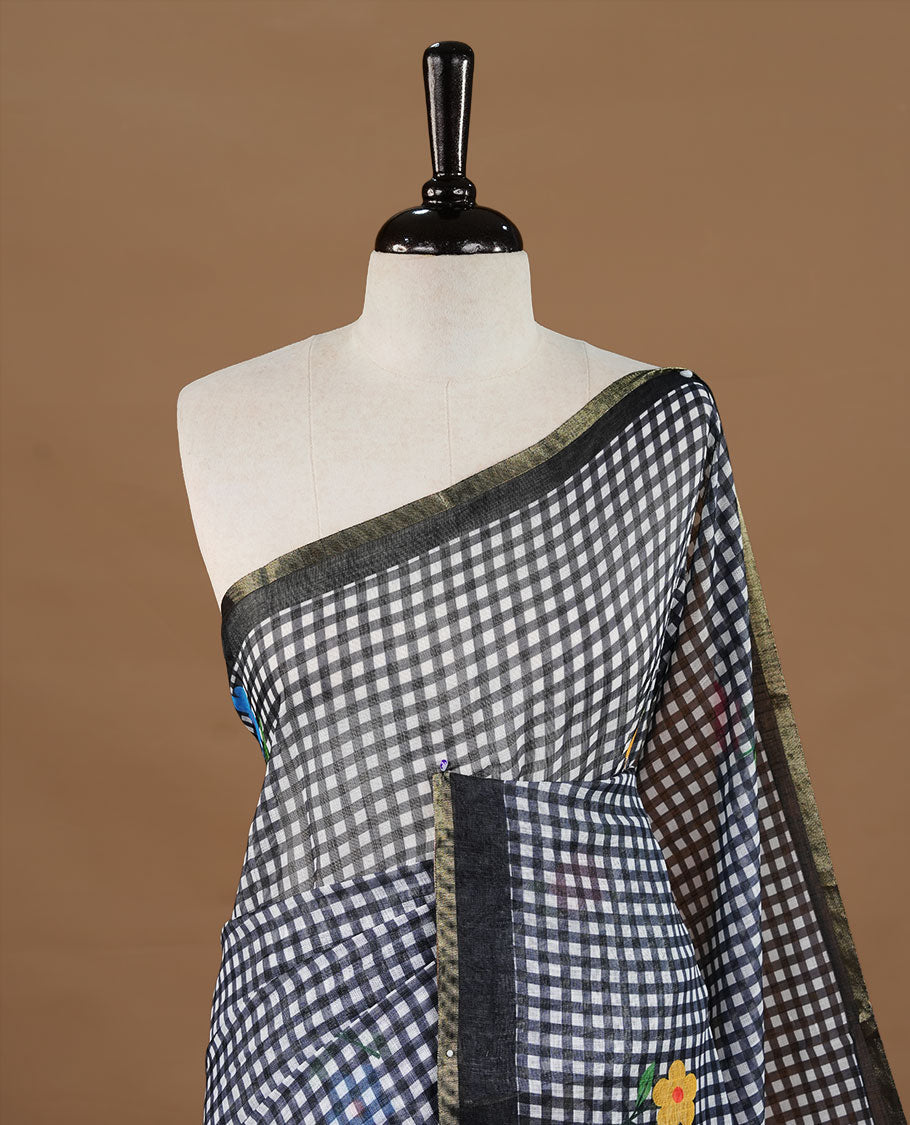 Black colour Semi Linen saree featuring a stylish check pattern adorned with floral prints on the body, enhanced by a small gold border, paired with a matching blouse piece.