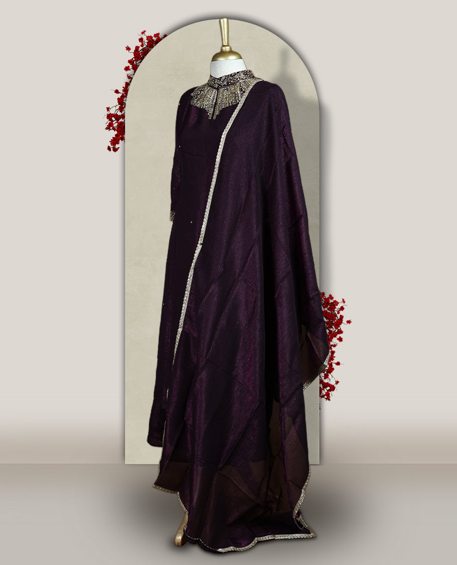 Deep wine colour churidar set with a rich sheen, beautifully adorned with golden cut beads work on the neckline and sleeve borders, Paired with a matching dupatta featuring a subtle zari edge, perfect for a regal festive look.