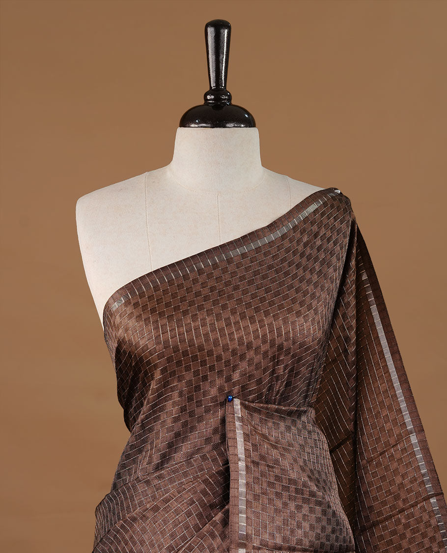 Brown colour Semi Tussar saree featuring an elegant zari fancy check pattern on the body, highlighted with a small border for a refined look. Comes without a blouse piece.