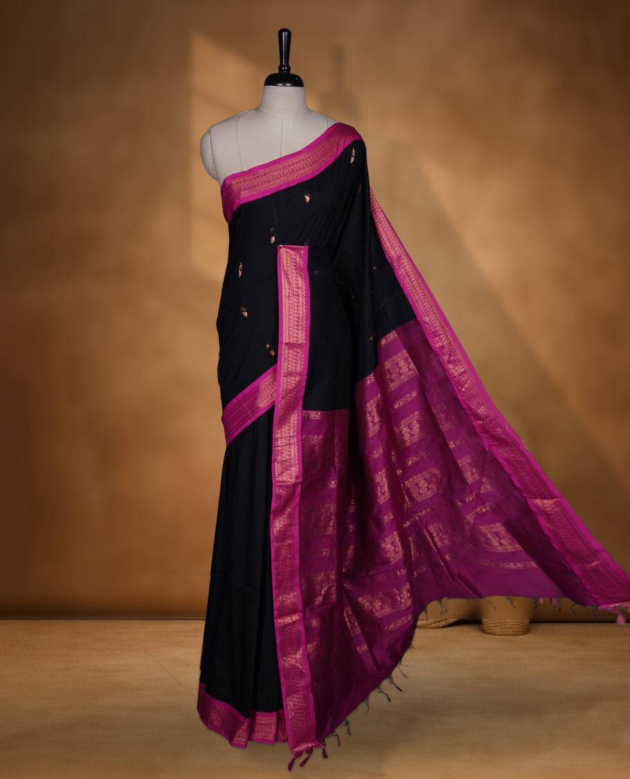Black colour Kalyani cotton saree featuring delicate zari buttas on the body, complemented by a magenta zari border and woven pallu, paired with a matching blouse.