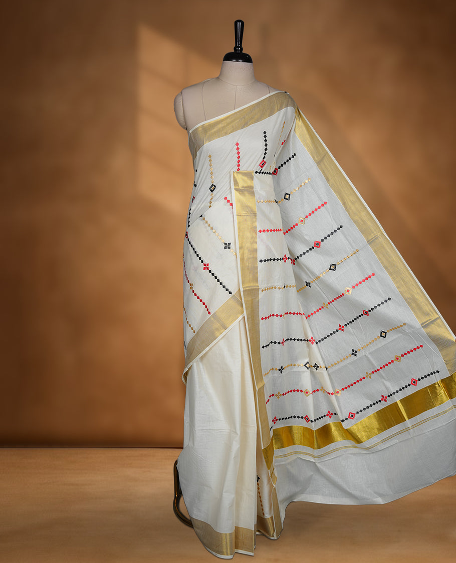 Off white Kerala saree featuring red and black geometric motifs, complemented by a classic golden zari border and traditional pallu, paired with a matching blouse.