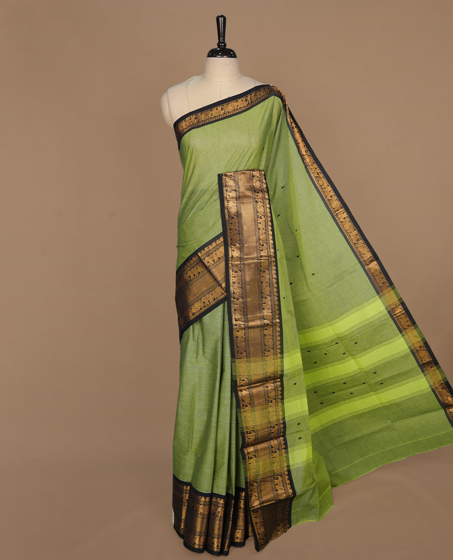 Green colour chettinad saree featuring gold zari motifs on body, complemented by contrast black colour with traditional border, paired with matching blouse piece.