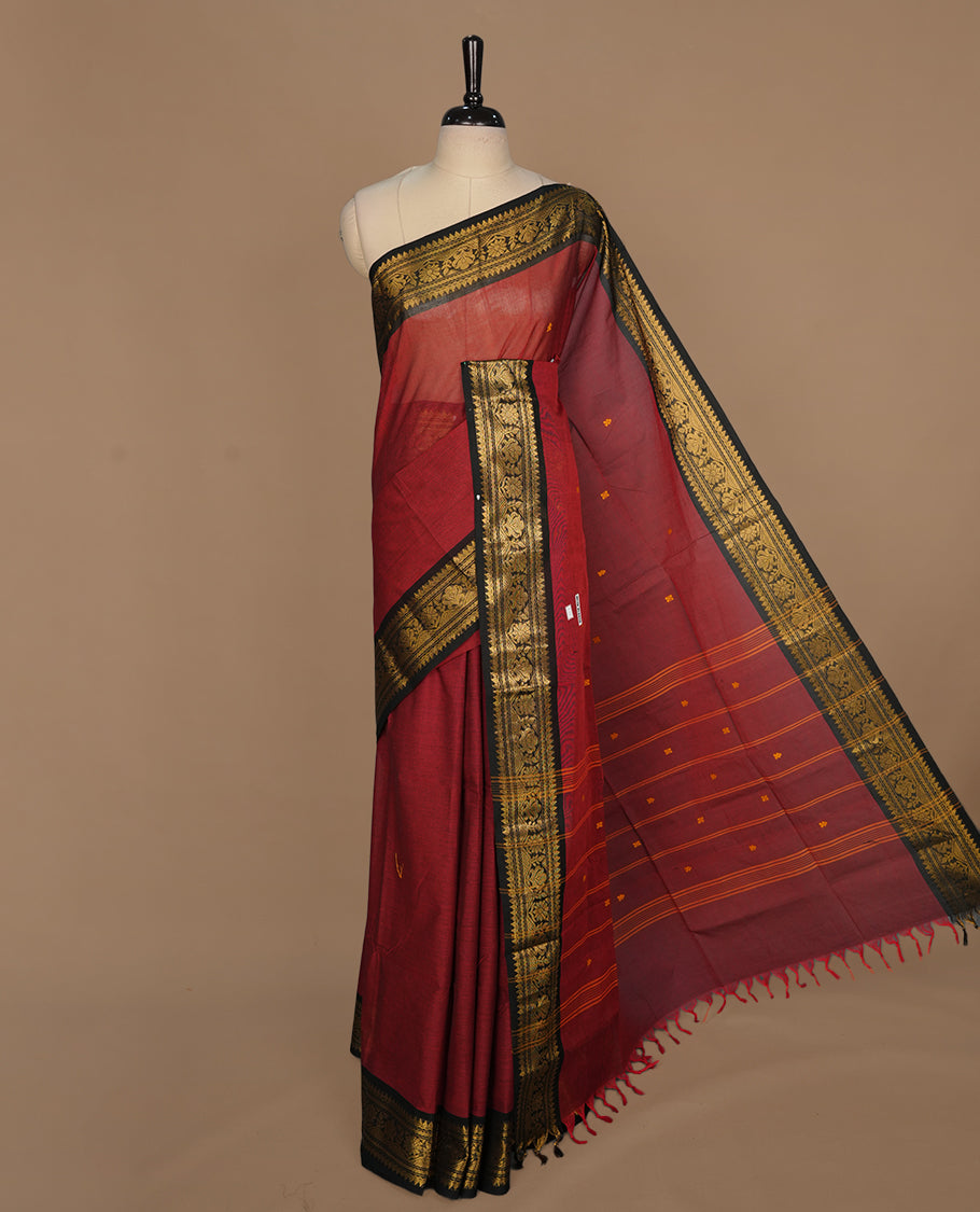 Maroon colour chettinad saree featuring gold zari motifs on body, complemented by contrast black colour with traditional border, paired with matching blouse piece.