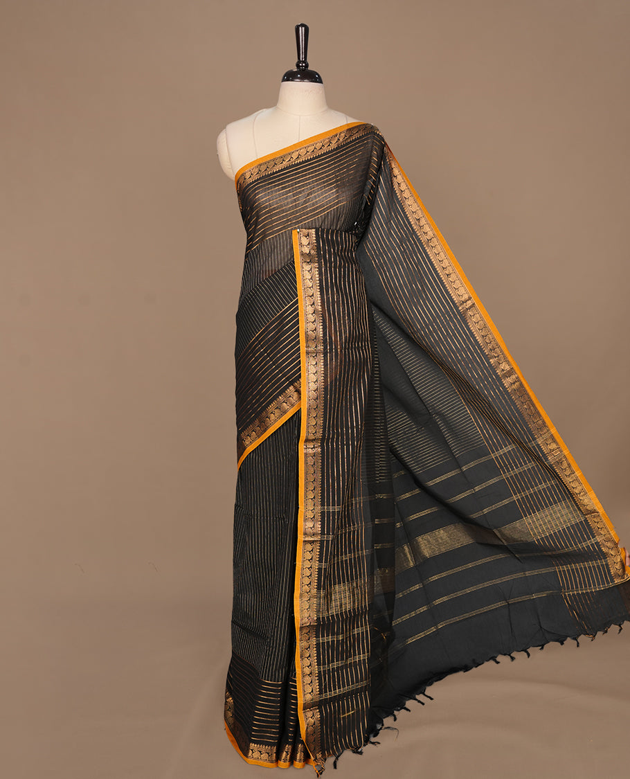 Black colour chettinad cotton saree featuring gold zari stripes on body, complemented by yellow piping with gold zari border, paired with matching blouse piece.
