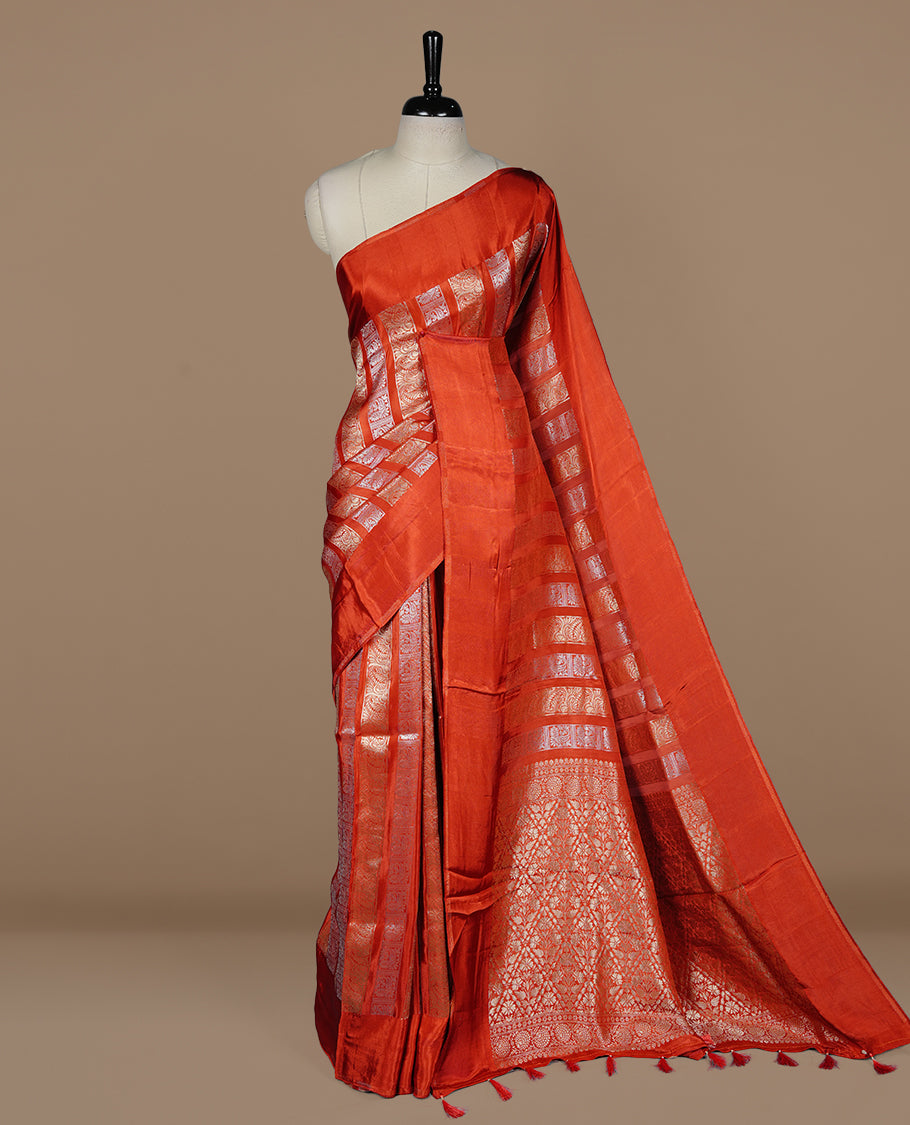 Brick red colour banaras crepe saree featuring gold & silver zari design stripes on body, complemented by self colour border, paired with matching blouse piece.