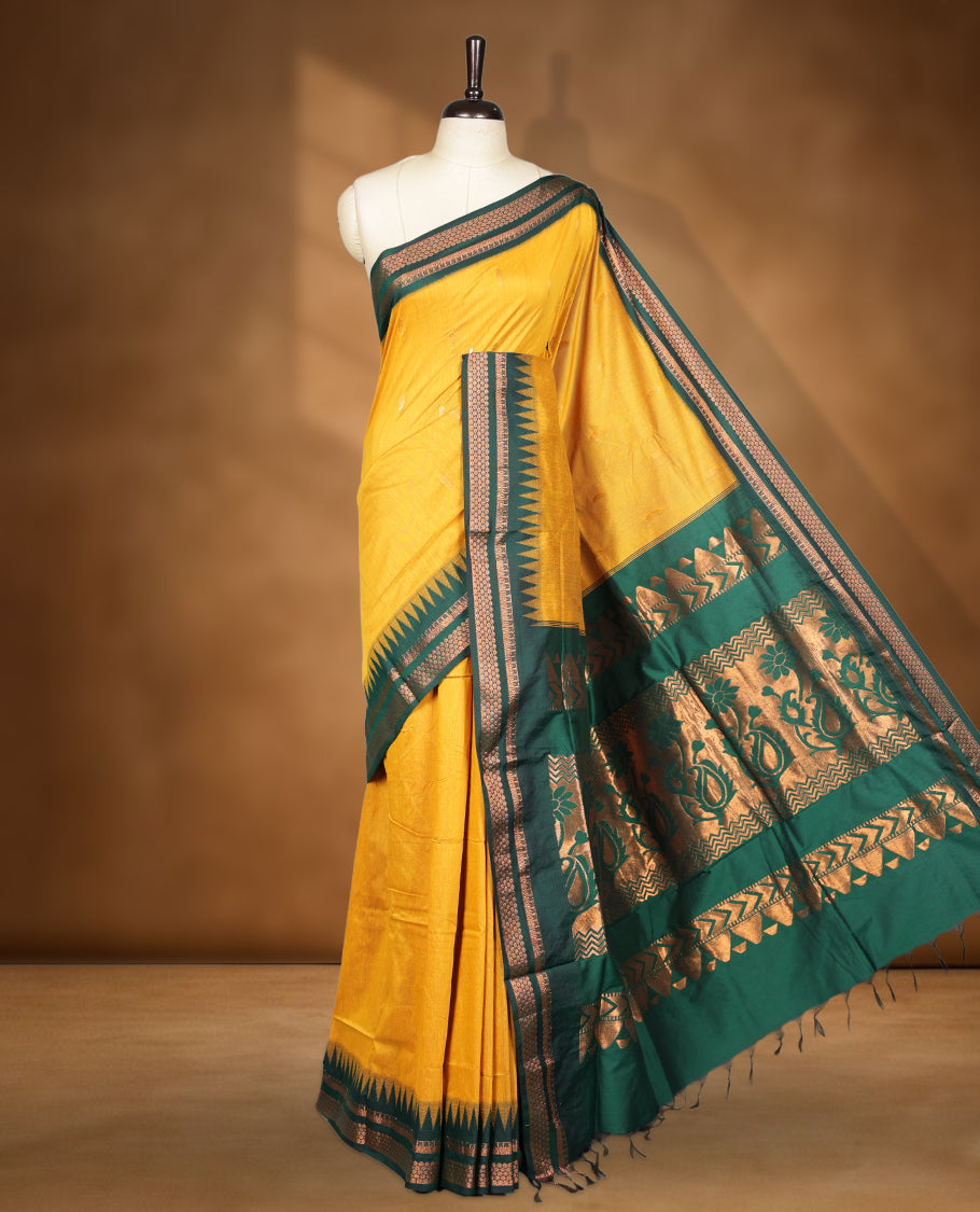 Mustard colour kalyani cotton saree featuring Antique zari motifs on body, contrast green colour border with geometric antique zari pattern, paired with matching blouse piece.