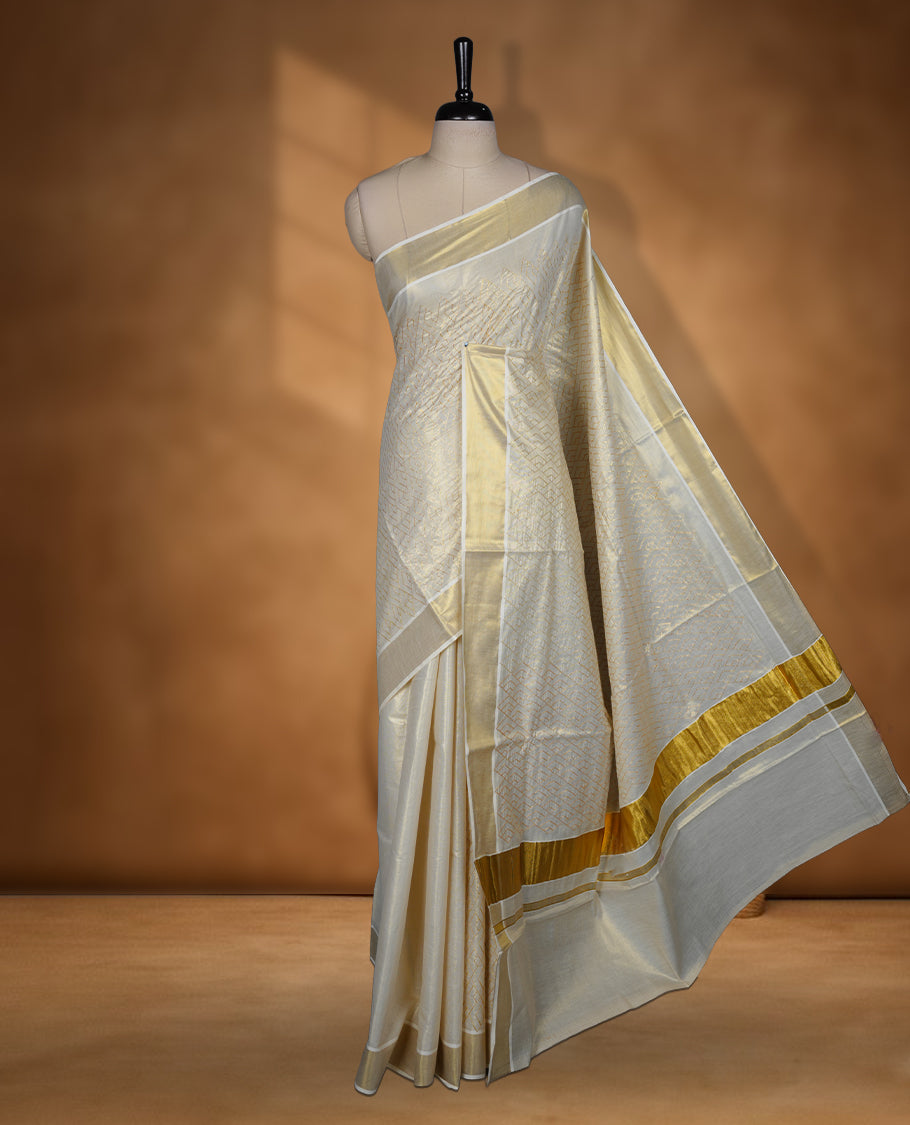 Off white colour Tissue Kerala saree featuring an elegant all-over zari patterned body, complemented by a rich golden zari border and traditional pallu, paired with a matching blouse.