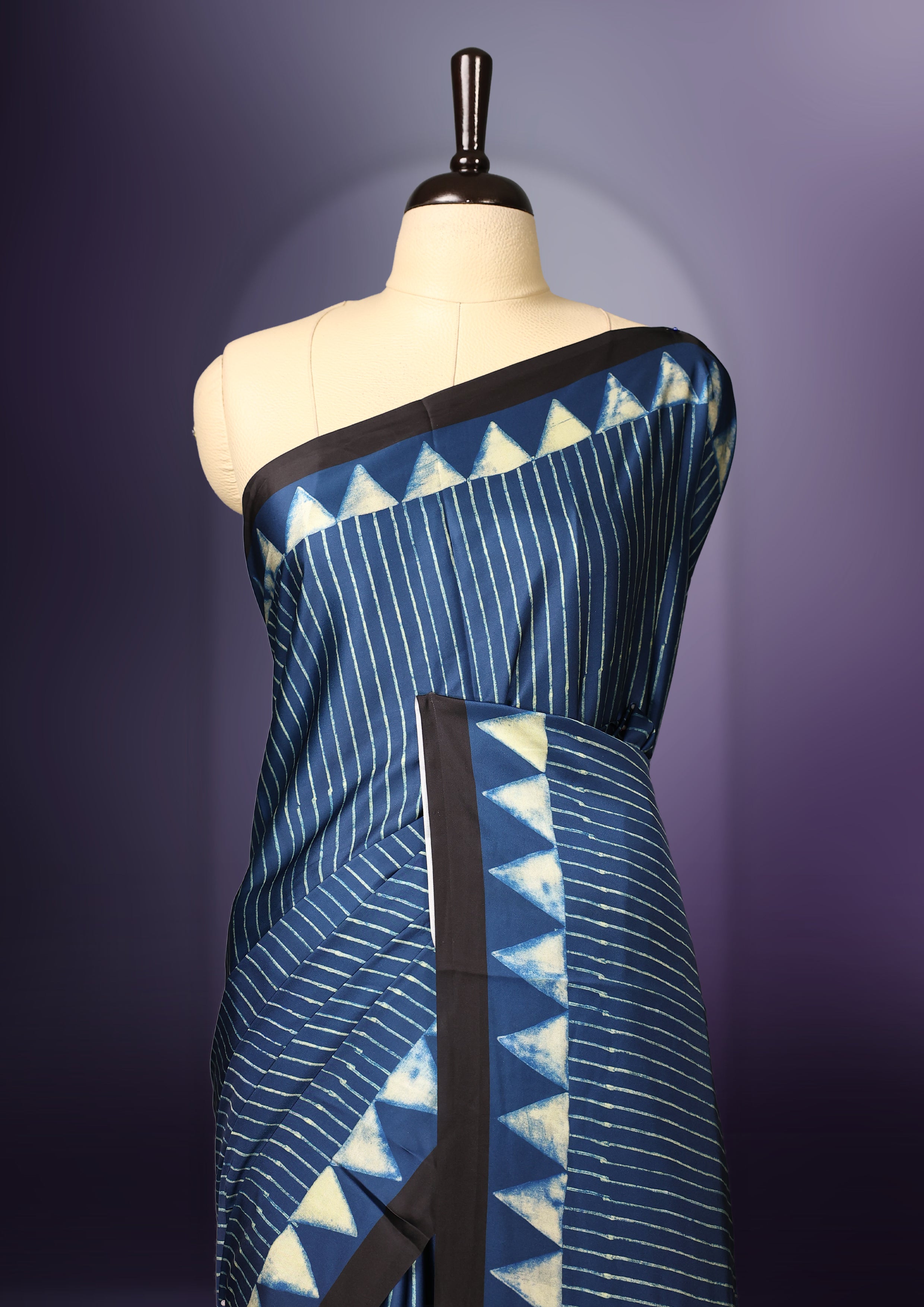 Blue colour saree featuring fine striped patterns across the body, accentuated with bold triangular designs along the border, and a contemporary pallu with geometric detailing, paired with a matching blouse.