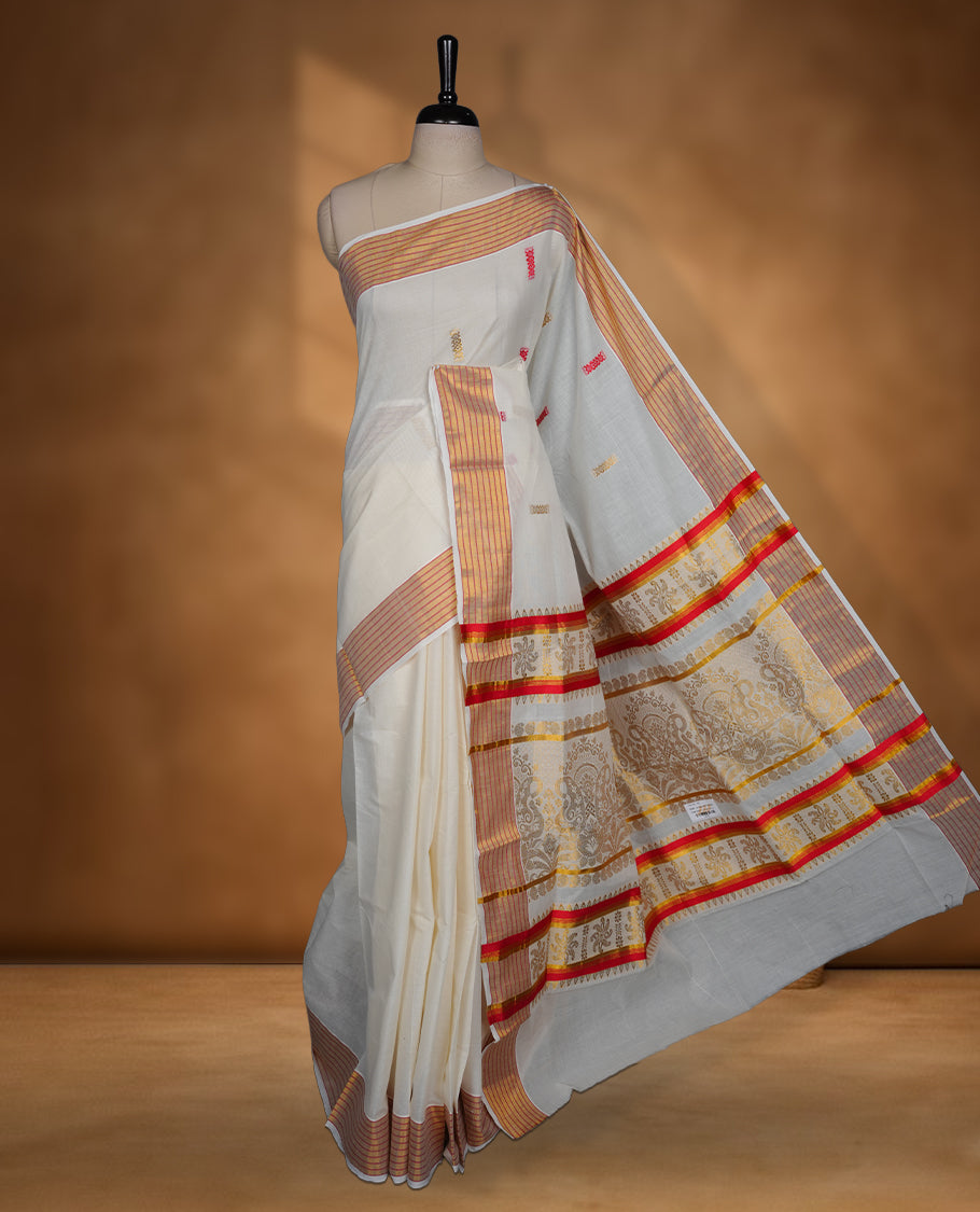 Off white colour cotton Kerala saree featuring subtle woven motifs, striped zari border with red detailing, and rich traditional zari pallu, paired with a matching blouse.