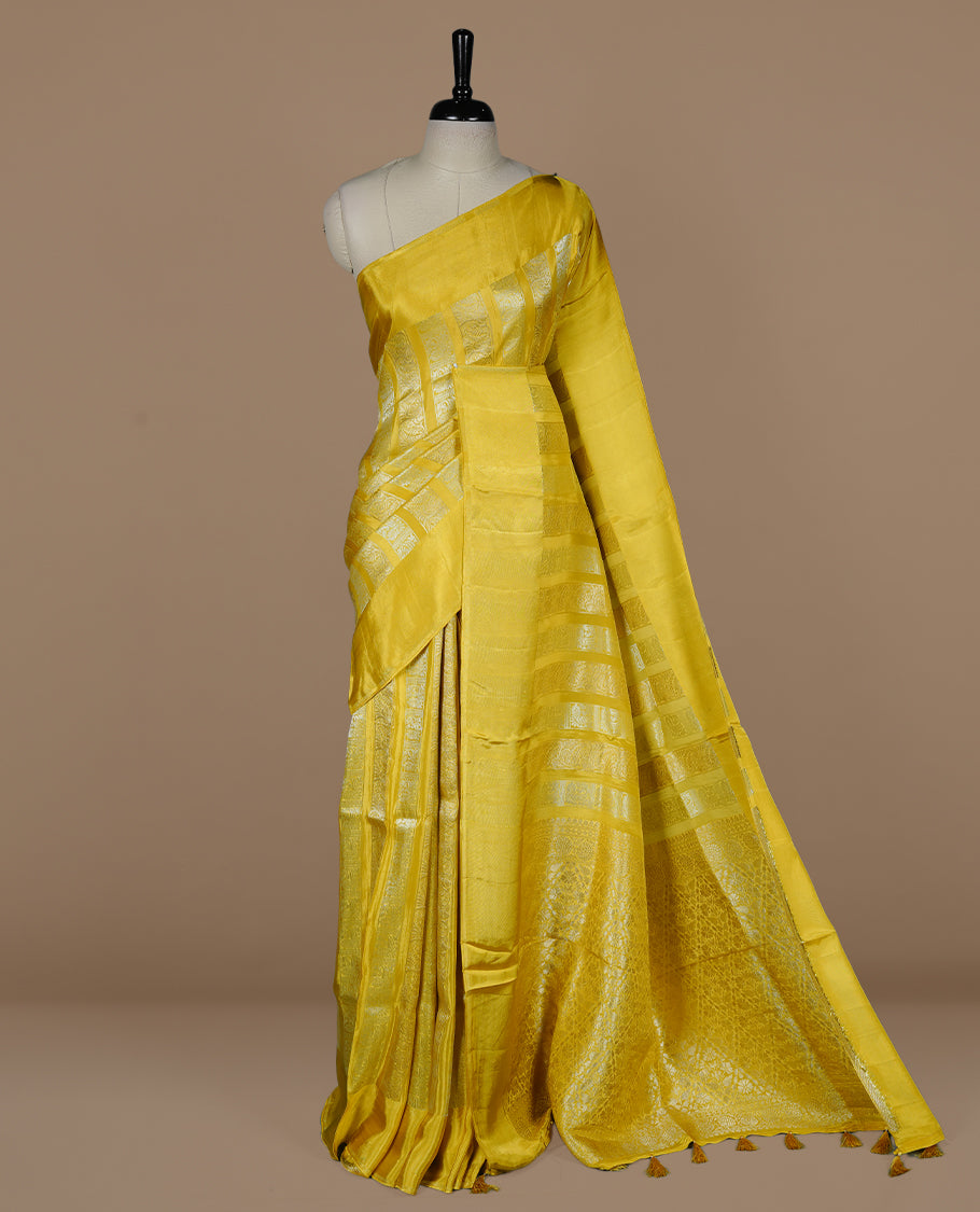 Yellow colour banaras crepe saree featuring gold & silver zari design stripes on body, complemented by self colour border, paired with matching blouse piece.