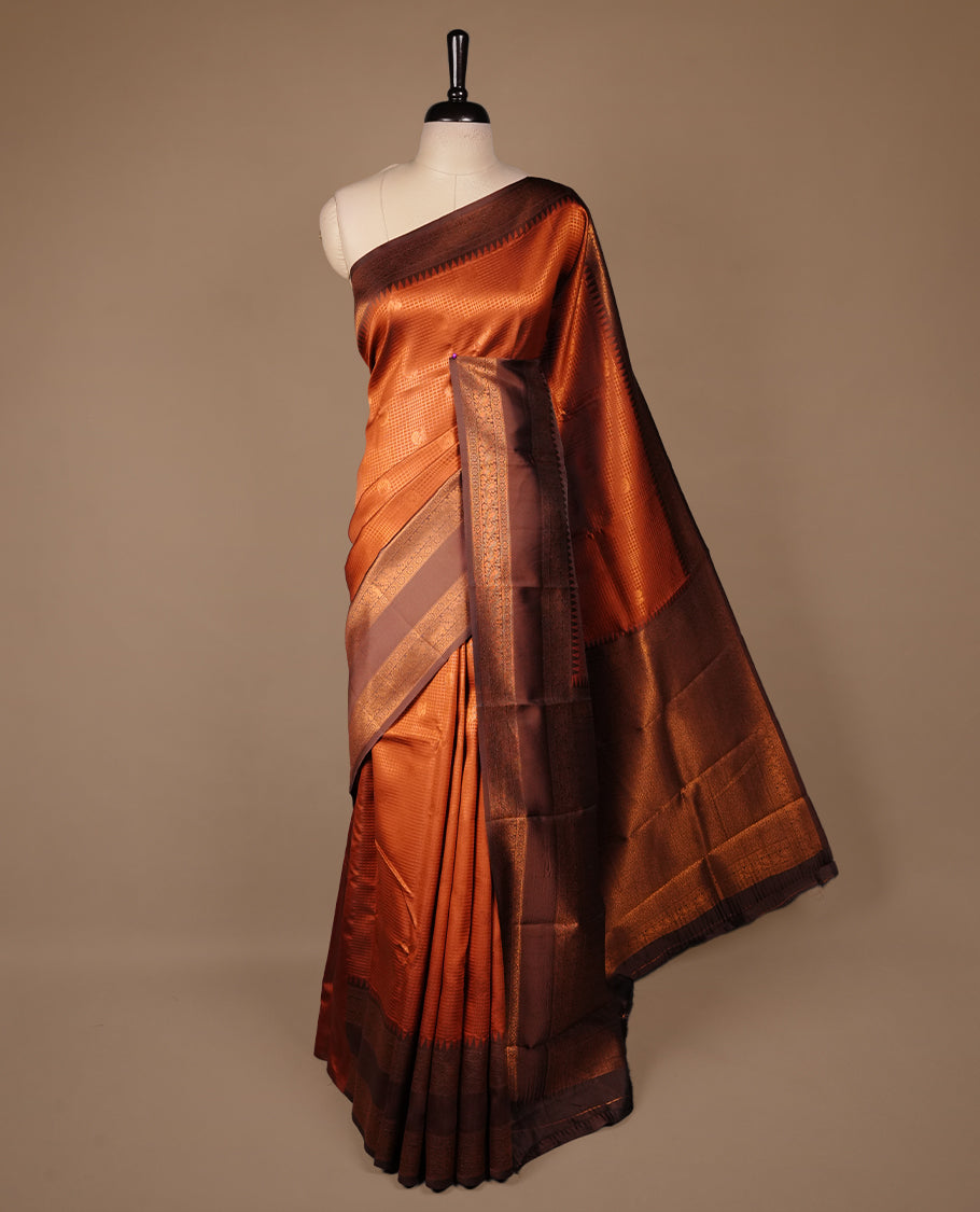Burnt orange colour silk saree featuring gold zari small square and motifs on body, complemented by contrast chocolate with traditional border, paired with matching blouse piece.