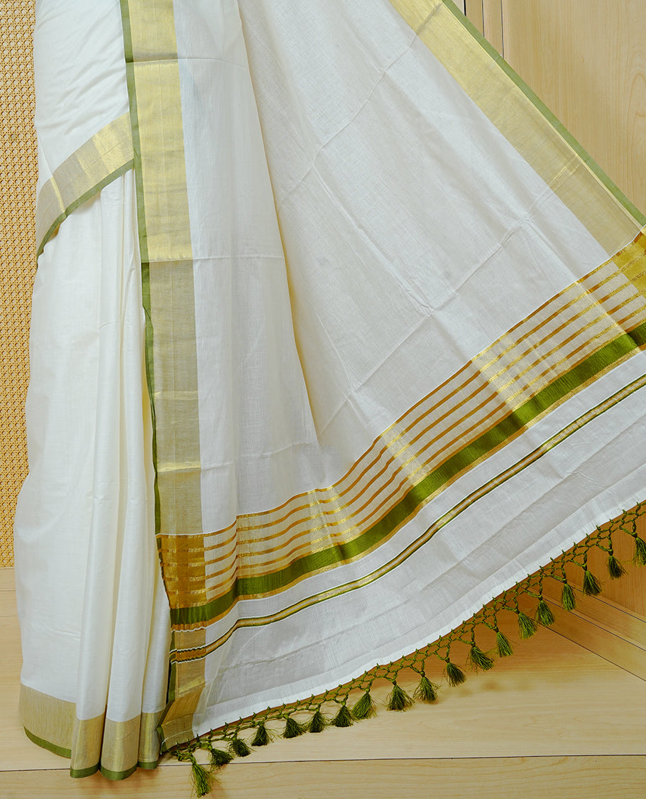 Cream Colour Cotton Kerala Saree Featuring A Plain Body, Enhanced With A Gold Zari & Light Green Colour Border, A Traditional Gold Zari Pallu, Light Green Tassels, And A Matching Blouse Piece.