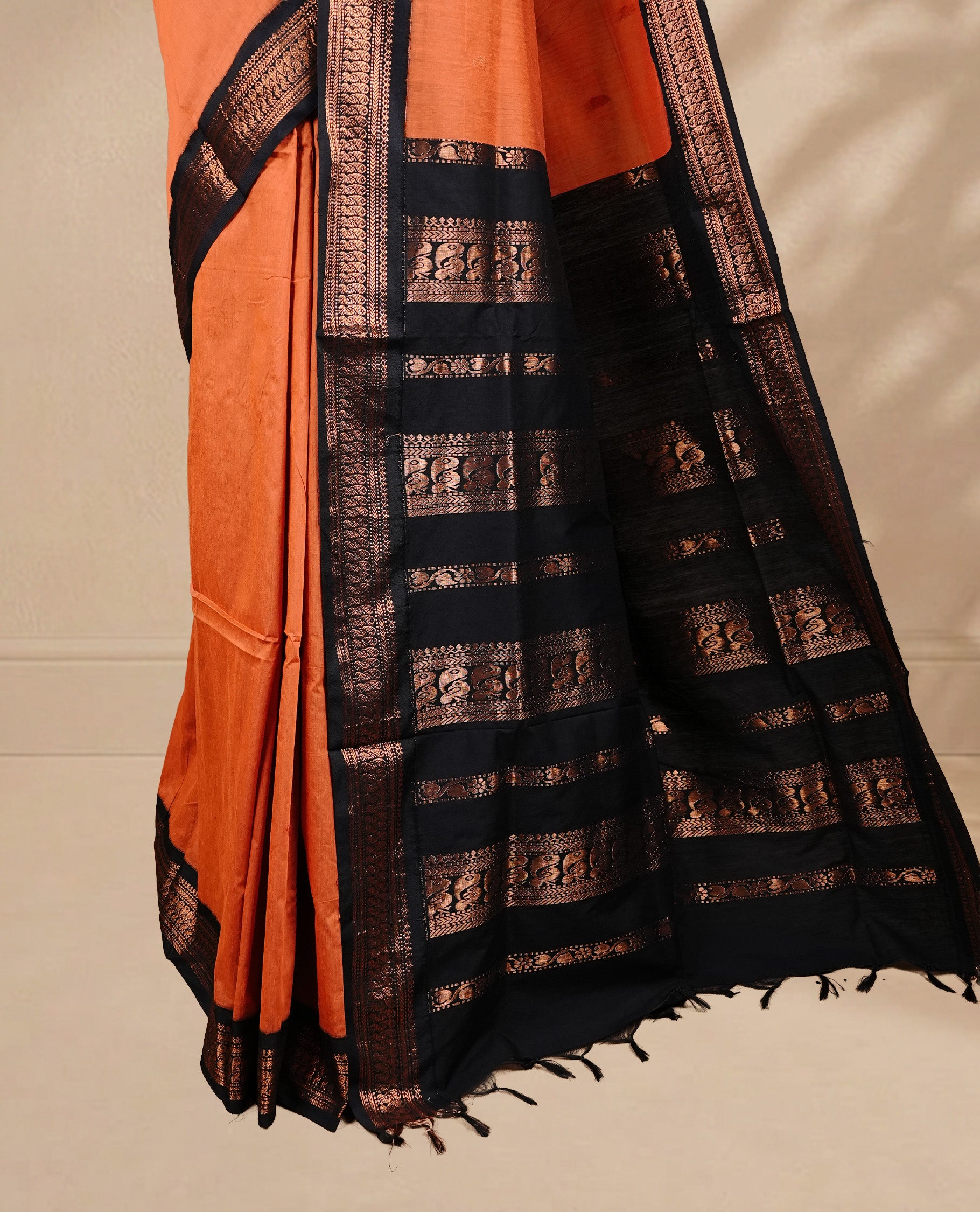 Orange colour kalyani cotton saree featuring antique zari motifs on body, complemented by Black colour with Antique zari border, paired with matching blouse piece.