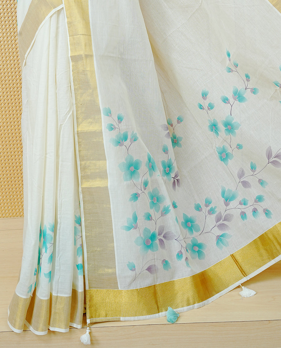 Cream Colour Cotton Kerala Saree Featuring Digital Floral Prints Across The Body, Enhanced With A Gold Zari Border, Traditional Gold Zari Pallu, Finished With Mint & White Tassels And A Matching Blouse Piece