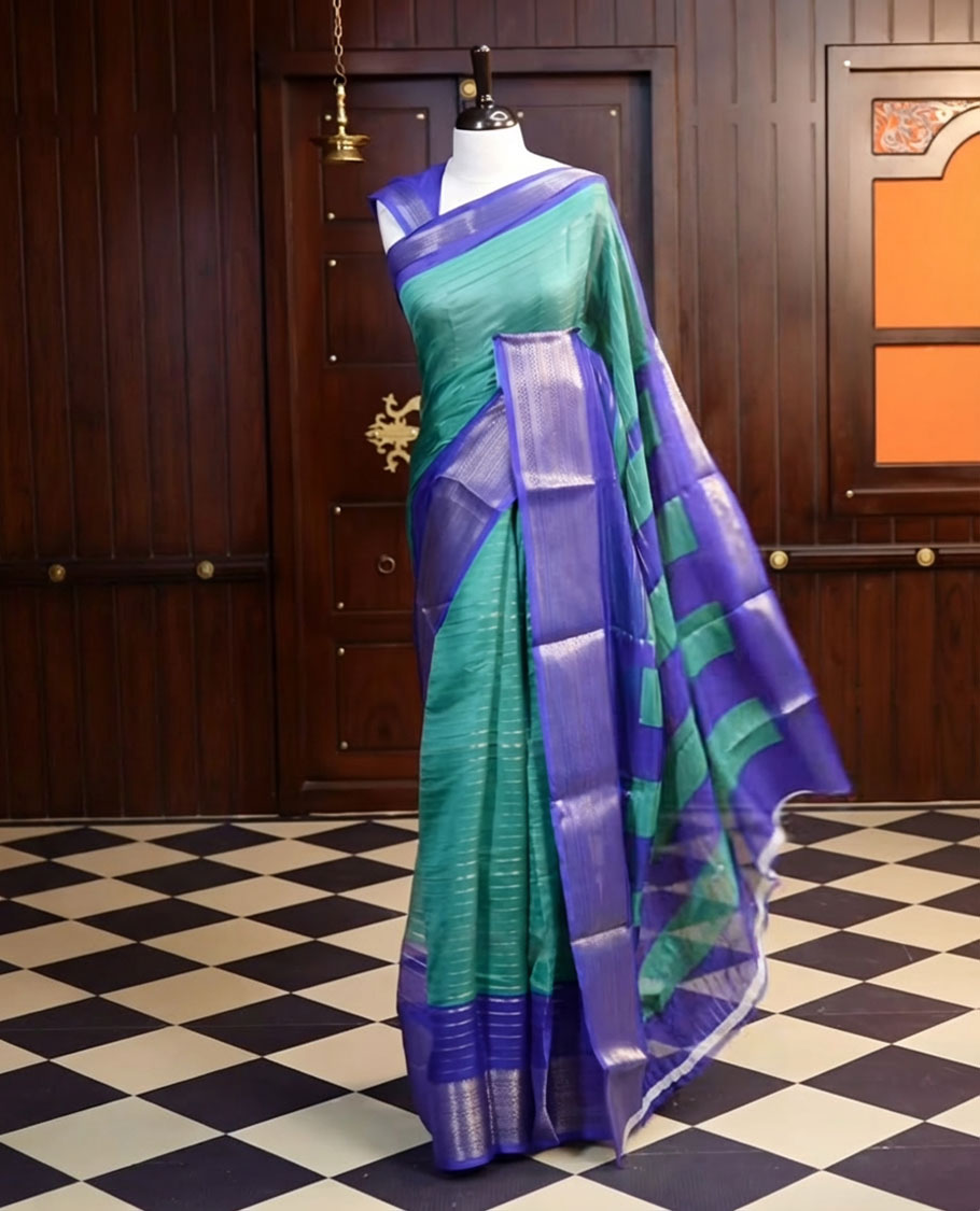 Teal Green colour semi Banarasi saree featuring elegant gold zari stripes on the body, a contrasting Royal Blue border adorned with intricate gold zari work, and a rich pallu, Paired with a matching blouse