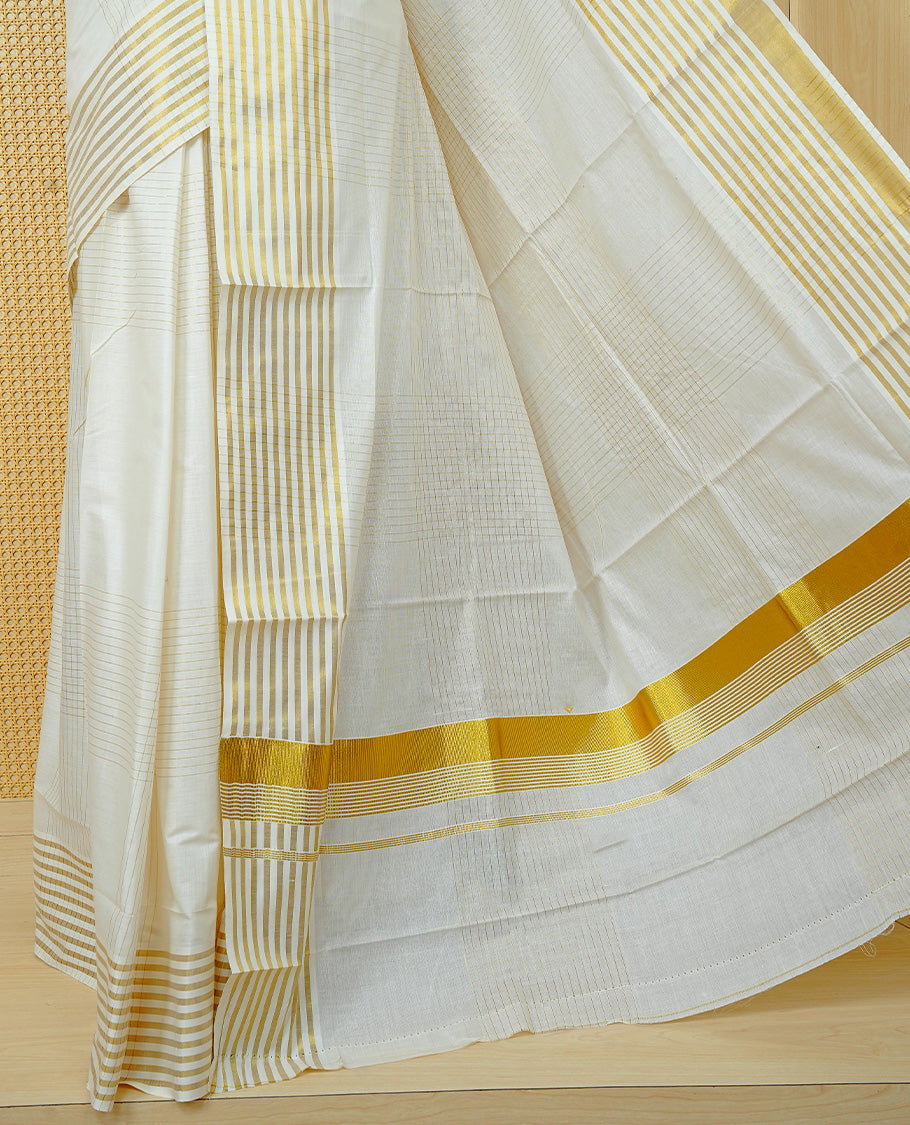 Cream Colur Cotton Kerala Saree Featuring Gold Zari Strips Across On The Body, Classic Gold Zari Border & Pallu,Paired With A Matchinf Blouse Piece.