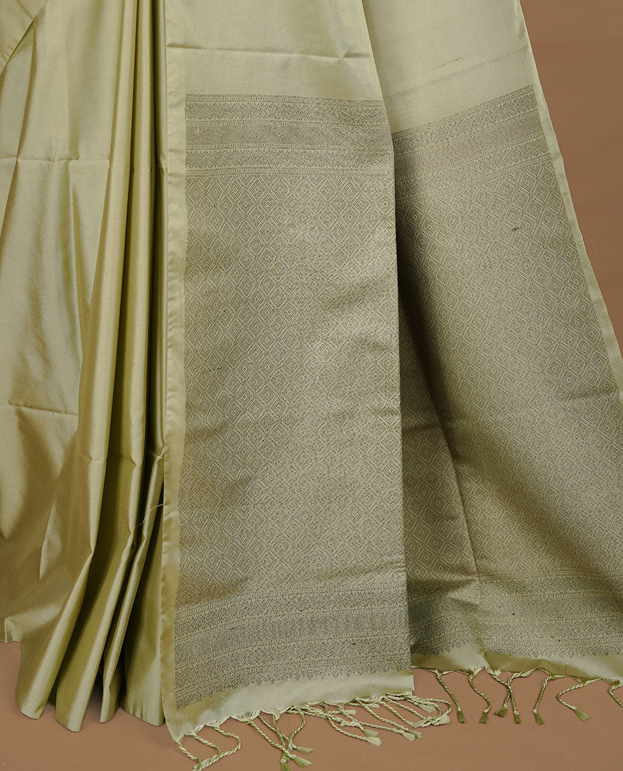 Tea green soft silk saree features a sleek borderless design with intricate antique zari motifs, flowing into a seamless self colored pallu and a matching blouse piece.