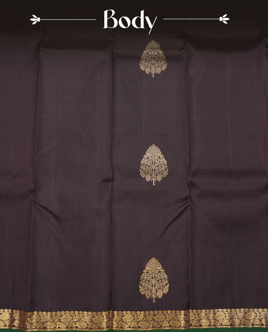 Deep coffee brown colour pure traditional Kancheepuram silk saree adorned with elegant zari tree motifs across the body, complemented by a rich zari woven border with a subtle green edge, paired with a matching blouse piece.