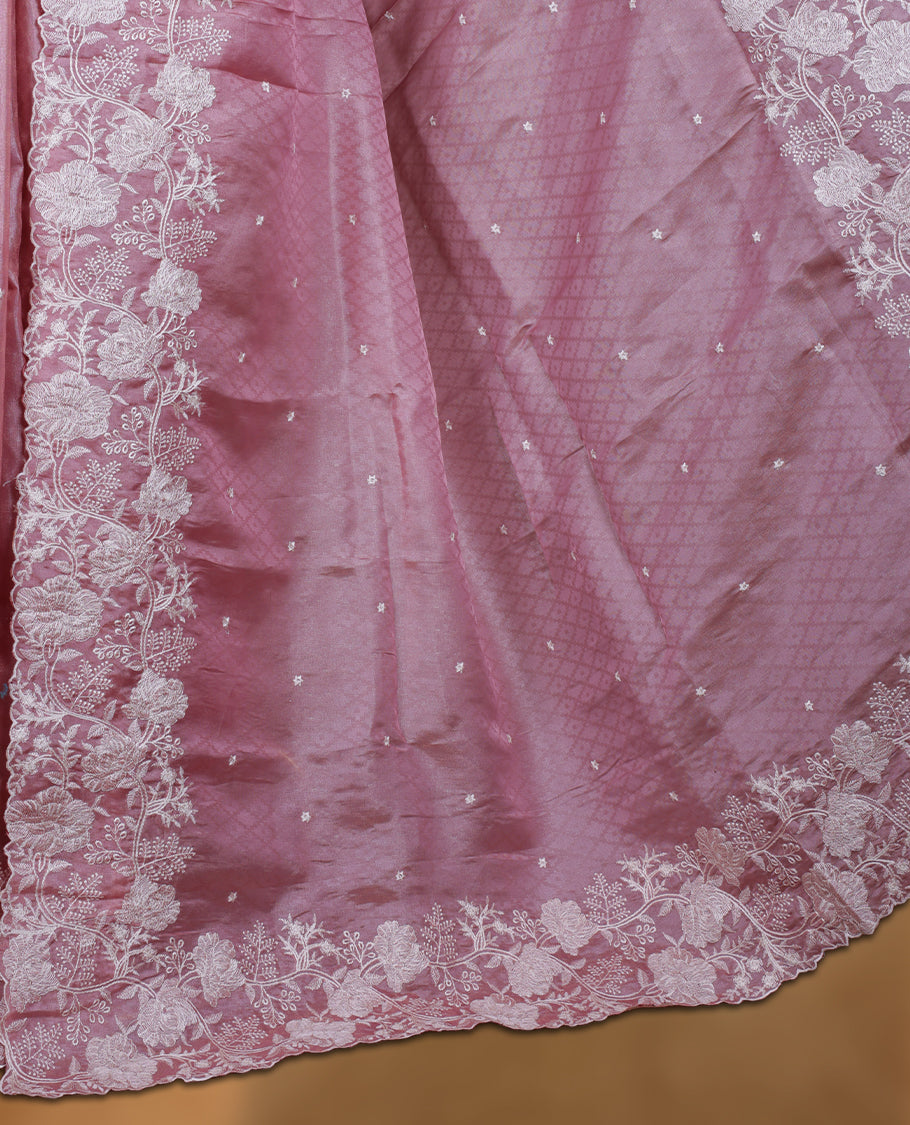 Pink colour organza designer saree featuring a subtle self patterned body and an intricately scalloped floral thread embroidered border all around, complemented by a coordinating embroidered pallu and paired with a matching blouse.