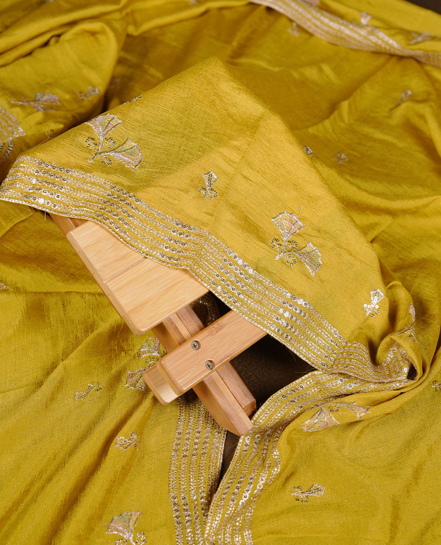 warm olive colour churidar material with subtle mirror and thread embroidery, finished with delicate border detailing and paired with a matching plain bottom and dupatta.