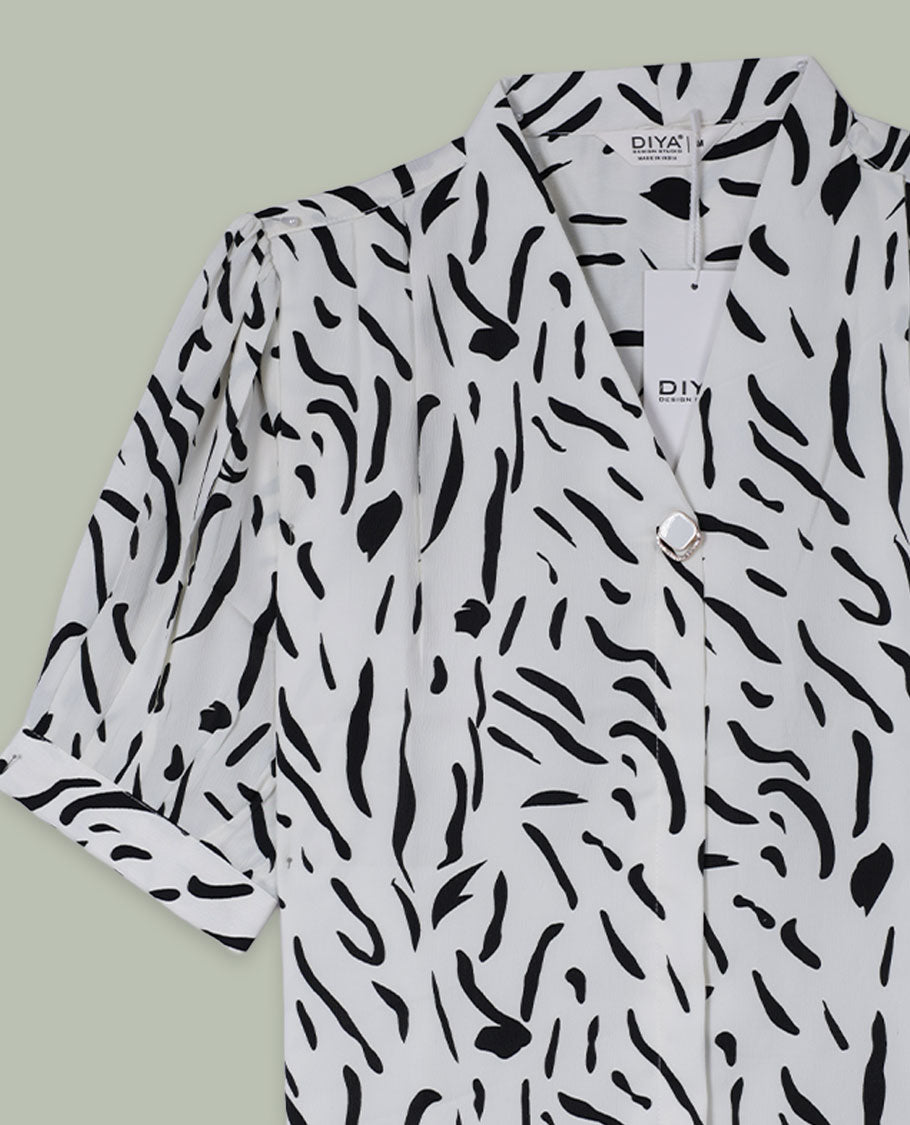White and black abstract printed shirt top with notched lapel collar, single visible button at front, elbow-length sleeves, and softly gathered shoulders.