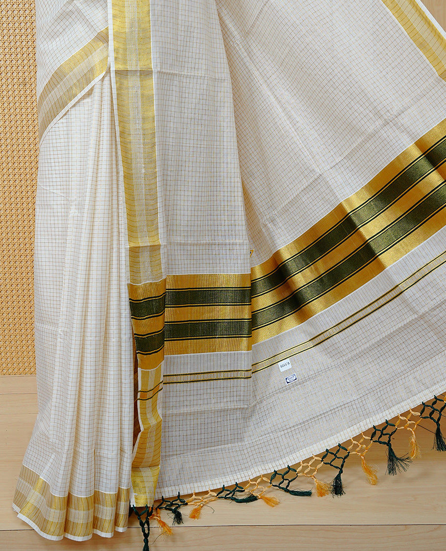 Cream Colour Cotton Kerala Saree Featuring A Golden Checks On Body, Enhanced With A Gold Zari Border, A Traditional Gold Zari & Green Pallu, Green & Golden Tassels, And A Matching Blouse Piece.
