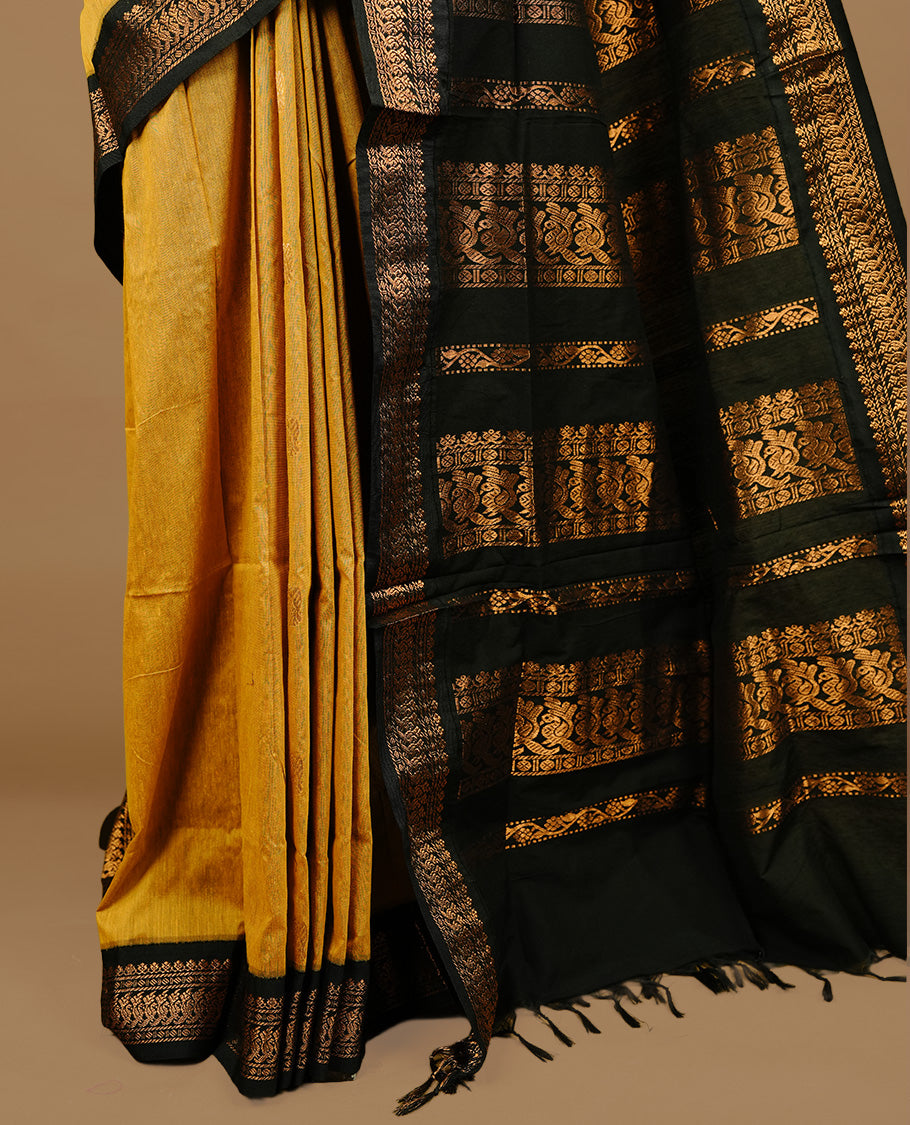 Mustard colour kalyani cotton saree featuring gold zari motifs on body, highlighting contrast Black colour with Antique gold zari border, paired with matching blouse piece.