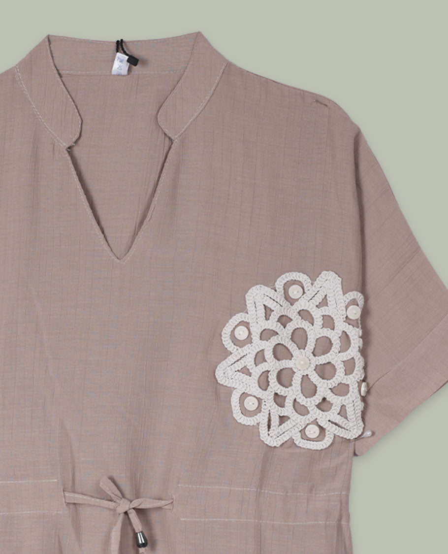 Taupe short-sleeve top with V-slit band neckline, contrast white crochet motif on one side, and adjustable drawstring detail at the waist