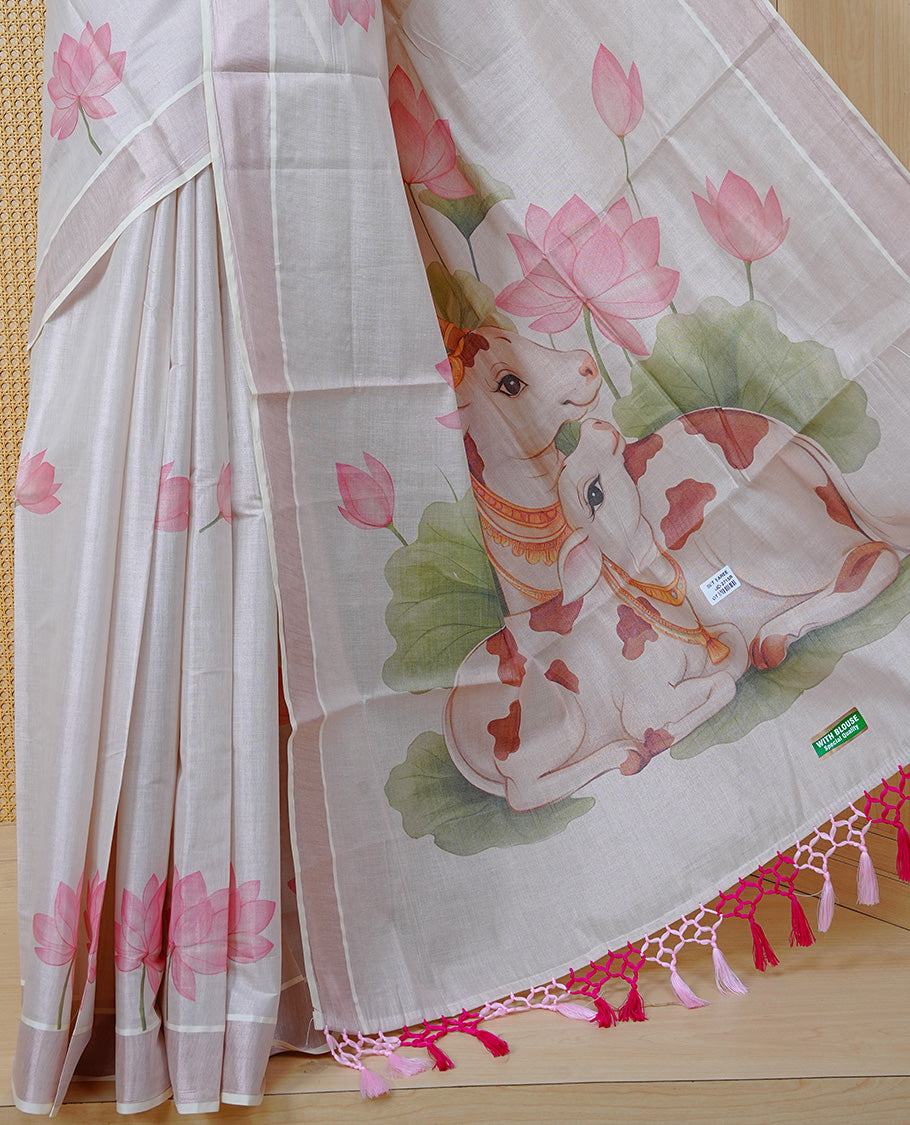 Cream Colour Tissue Kerala Saree Featuring Delicate Digital Lotus Prints And A Charming Cow & Calf Pallu, Enhanced With A Subtle Tissue Border And Contrast Pink Tassels. Paired With A Matching Blouse Piece.