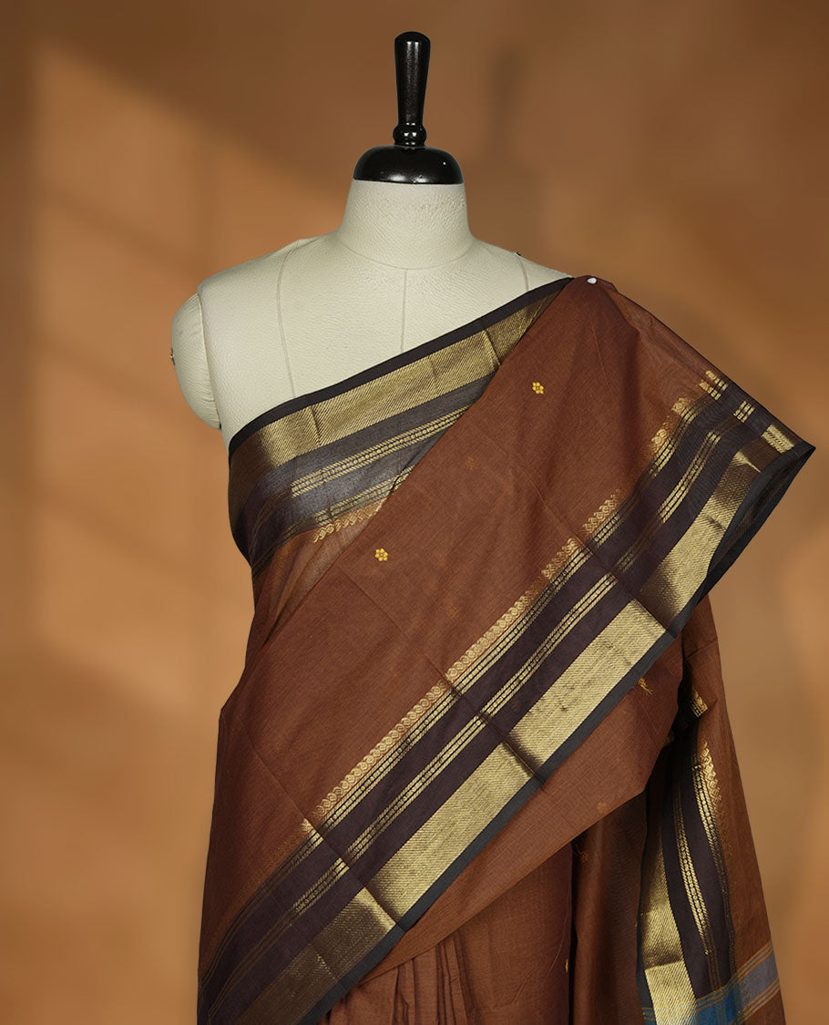 Brown colour chettinad cotton saree featuring small gold zari buttas on body highlighting contrast dark chocolate colour with gold zari traditional border, pallu and paired with matching blouse piece.